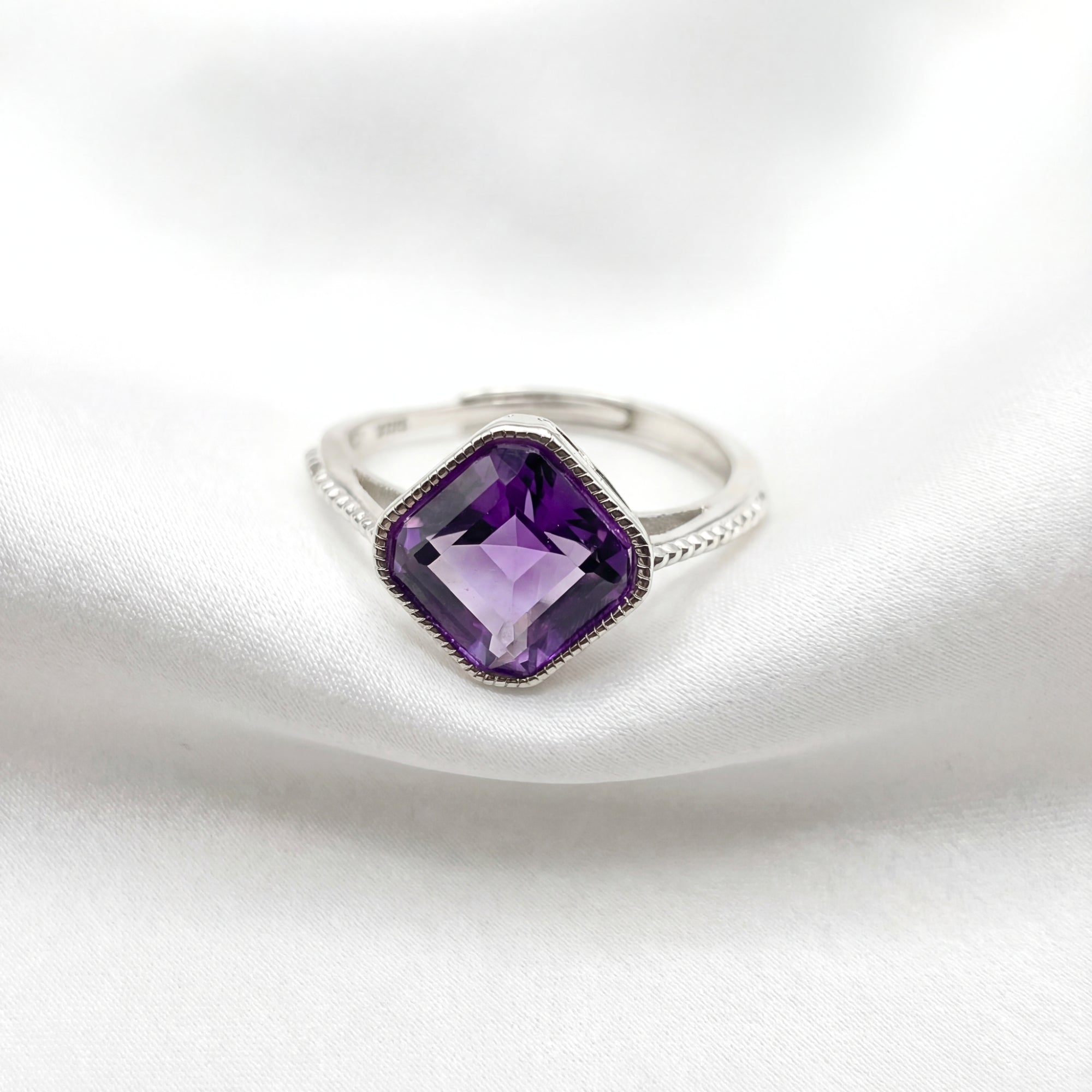 Cushion-cut simulated amethyst ring in S925 sterling silver with a textured band on white silk.