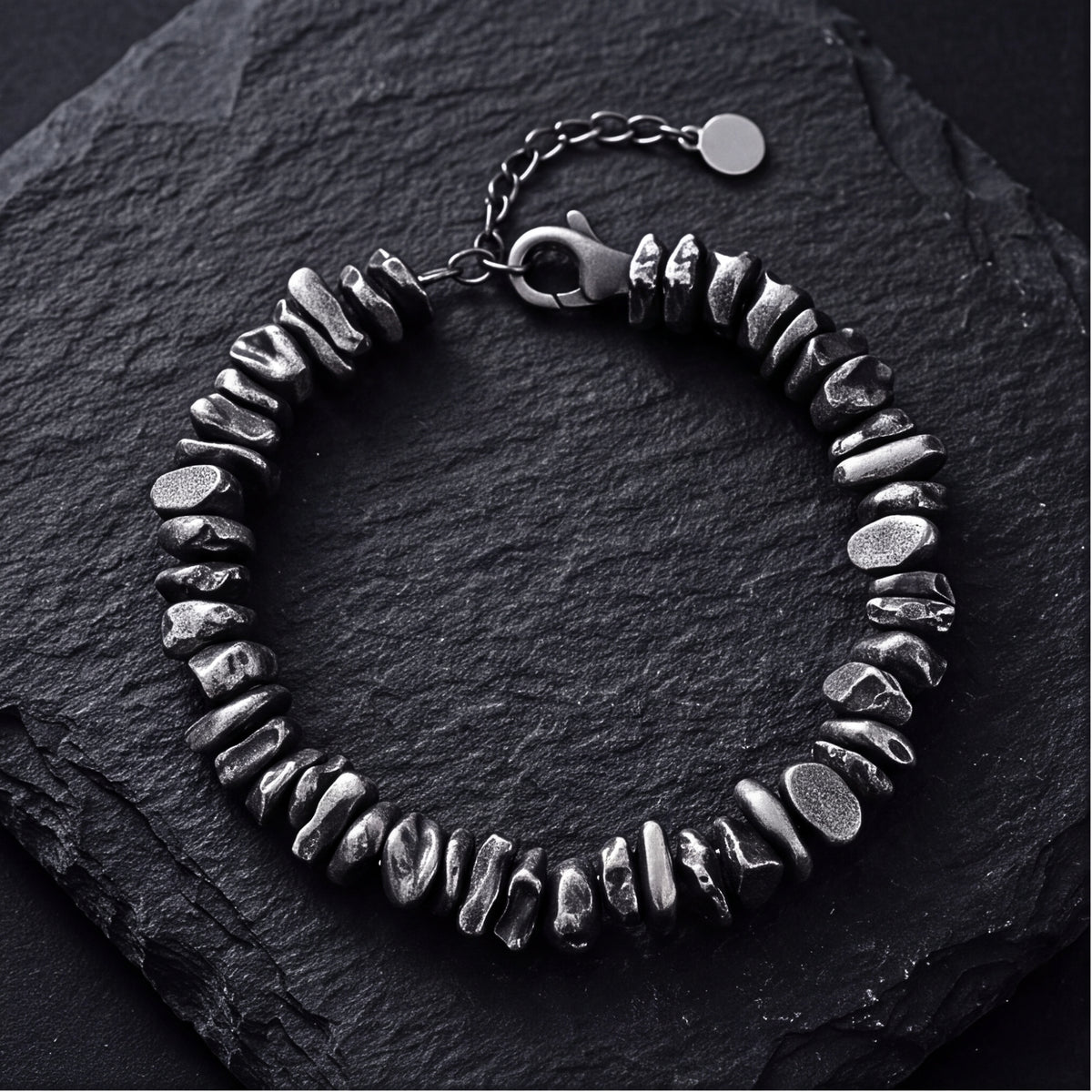Top-down view of a silver pebble link bracelet on dark slate, showing irregular links, clasp, and extension chain.