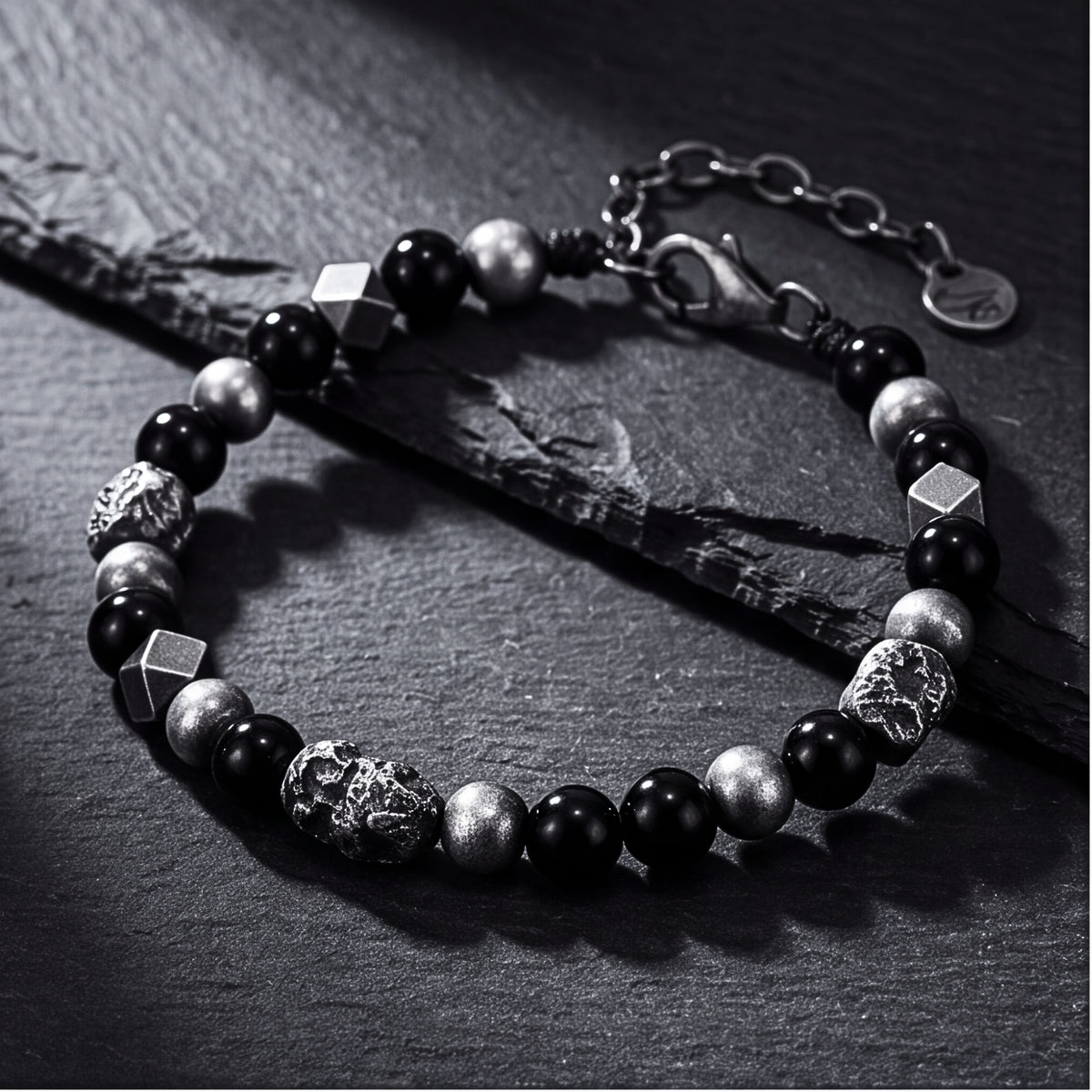 The Meteor Station Bracelet laid on dark slate, showing black beads, geometric silver accents, and clasp chain.
