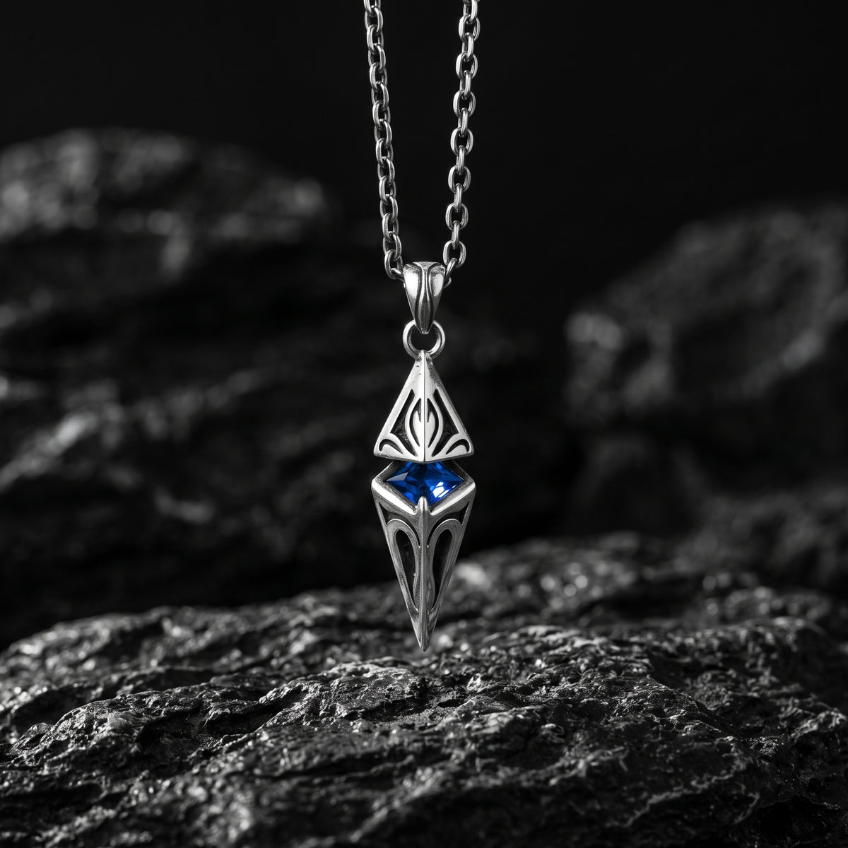 Silver geometric pendant with a vivid blue center stone hanging above a dark textured rock surface.