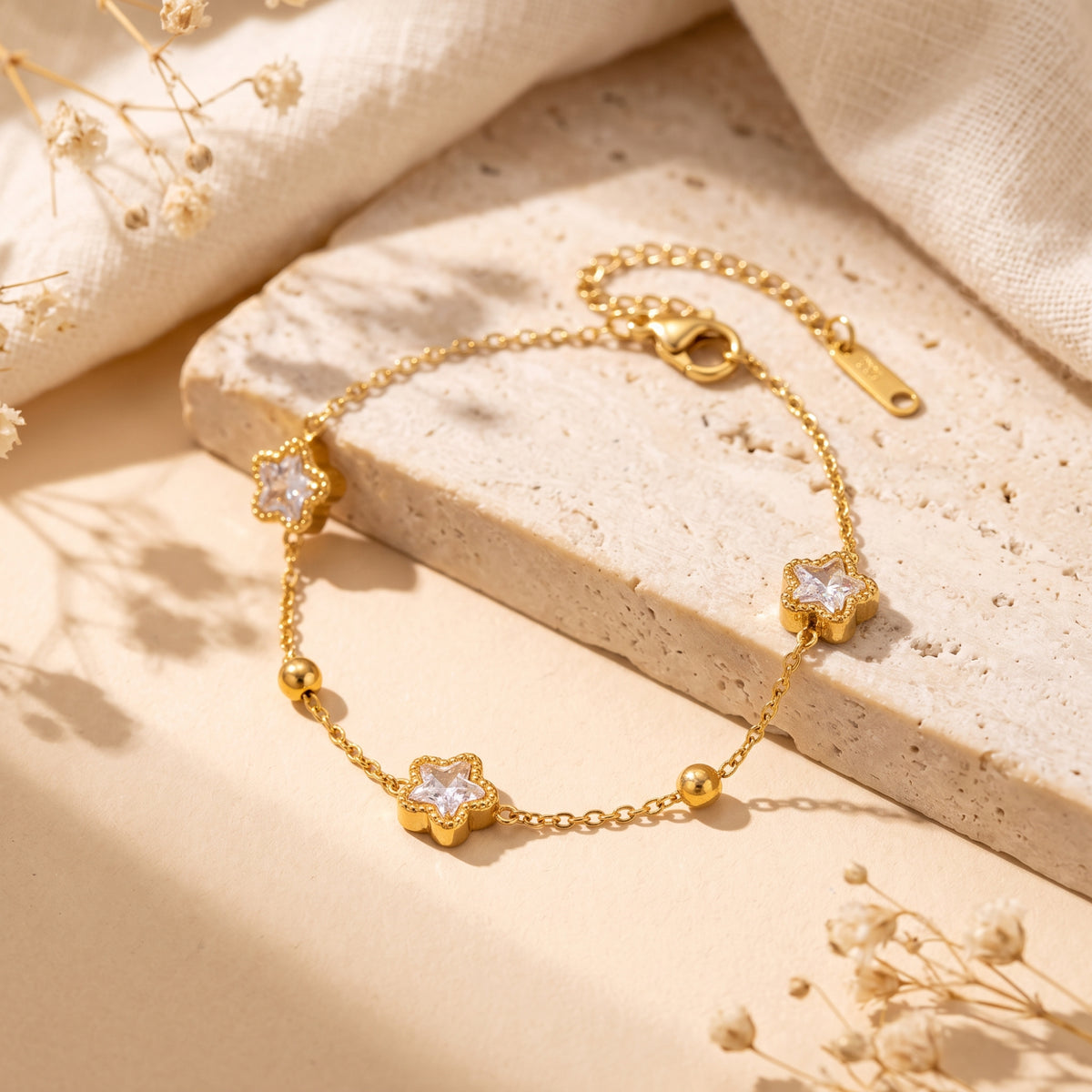 Gold-tone station bracelet with three star-shaped cubic zirconia stations on a stone slab with dried flowers.