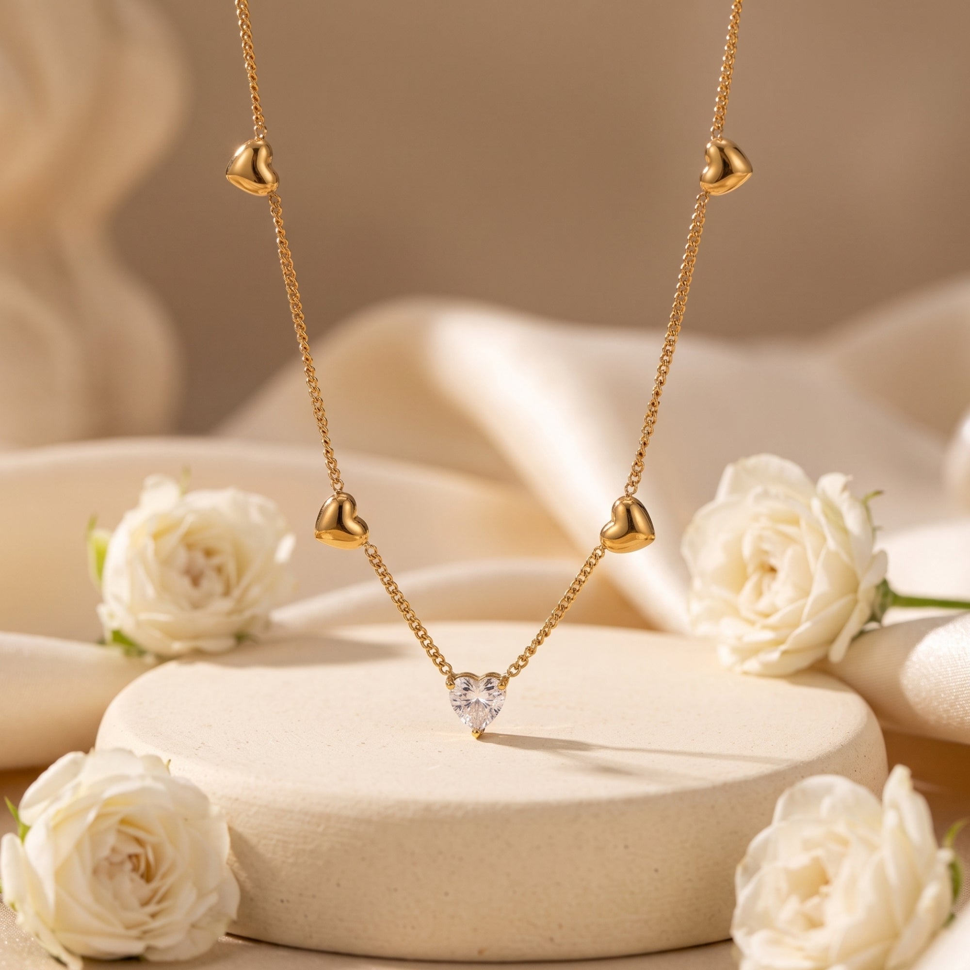 18K gold heart necklace with a heart-cut simulated diamond pendant displayed on a pedestal with white roses.