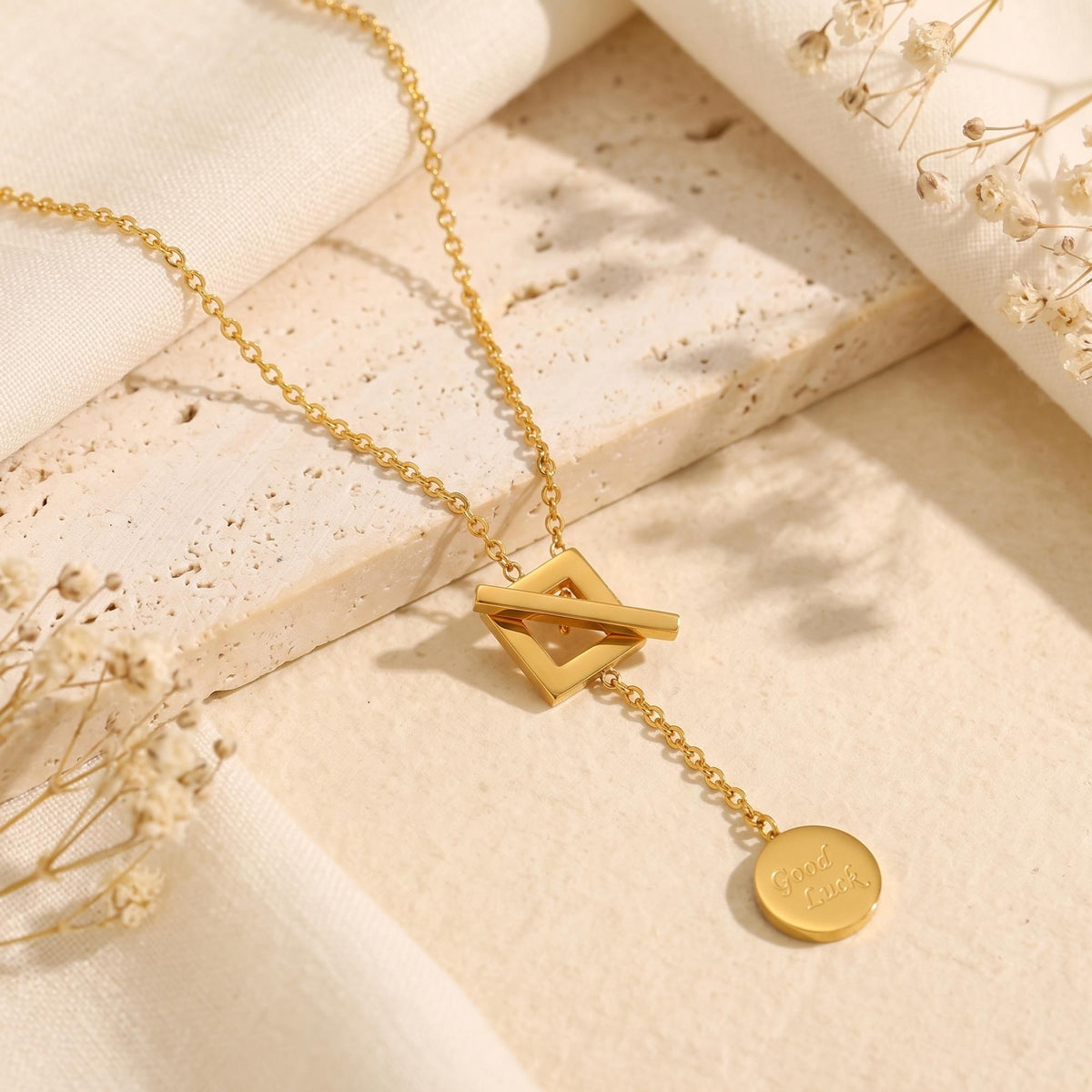Gold-tone lariat necklace with a square toggle clasp and hanging engraved Good Luck coin charm.