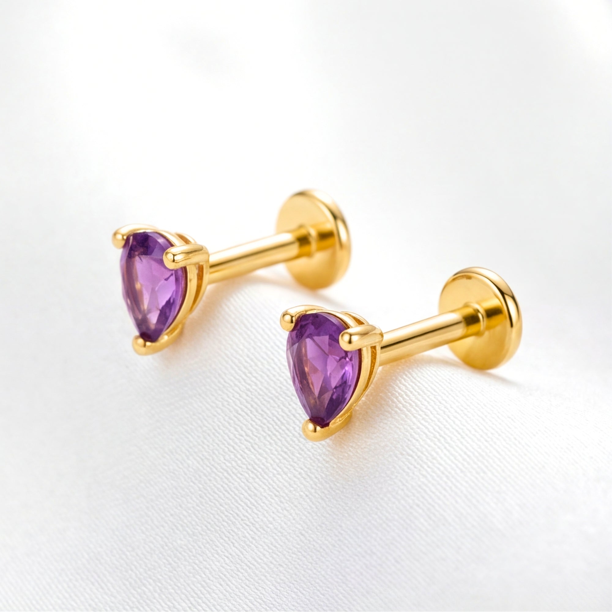 Purple pear cut simulated amethyst stud earrings in 18K gold vermeil with flat-back labret posts on white fabric.