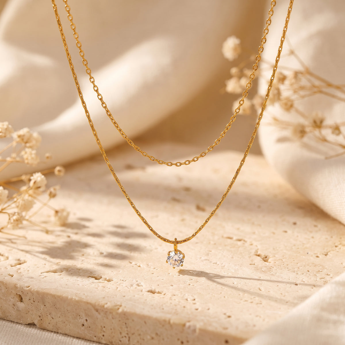 Gold-tone double-strand necklace with a round pendant draped over a light textured stone surface.