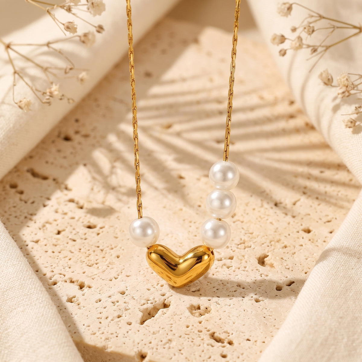 Close-up of the gold-tone heart necklace with asymmetrical pearls hanging over textured stone.