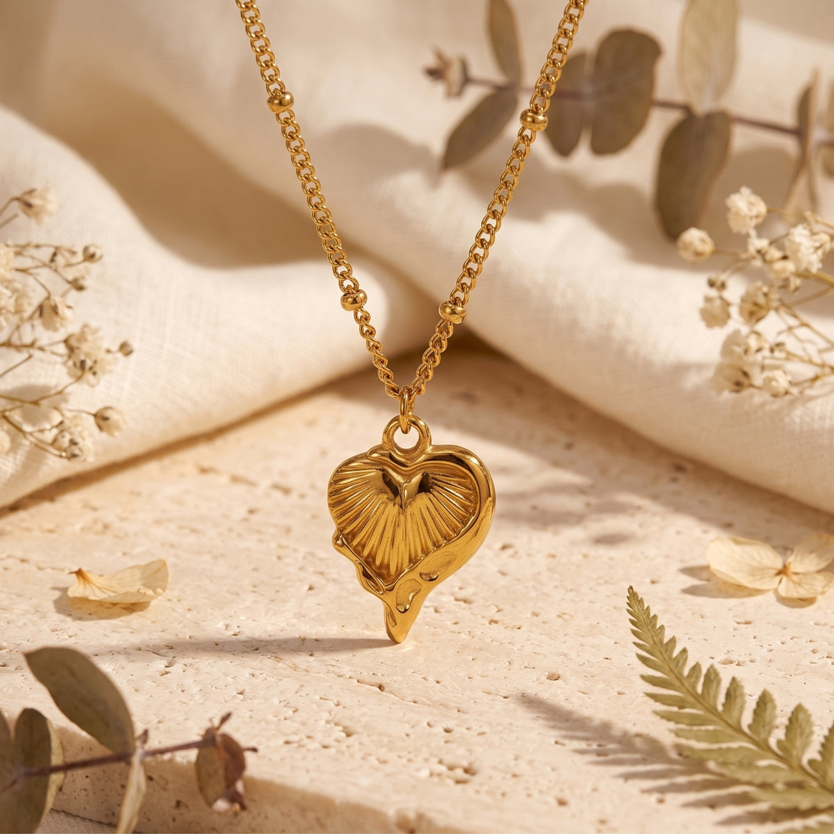 Gold-tone fluted heart pendant with a ribbed texture hanging vertically on a beaded satellite chain.
