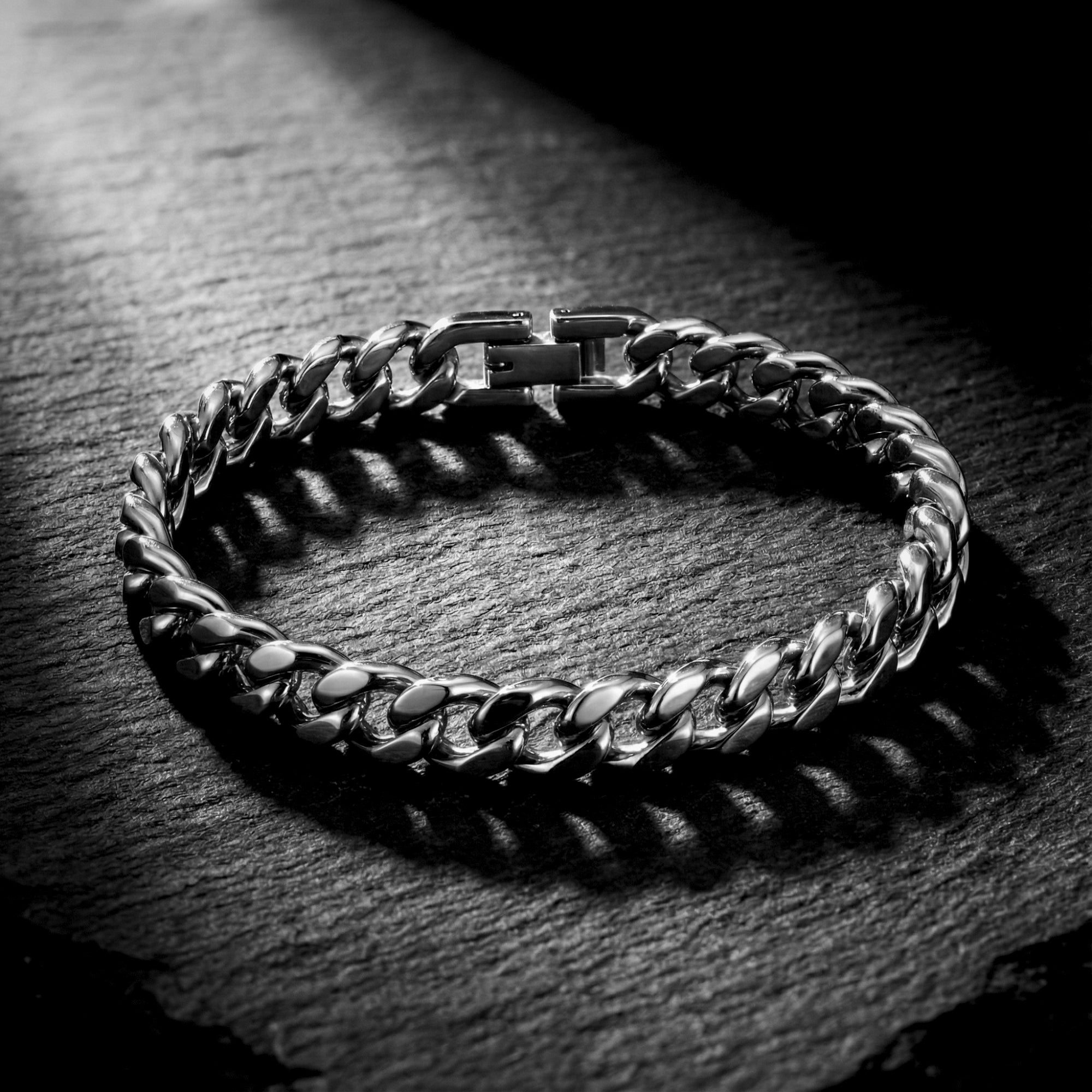 Silver stainless steel Cuban link bracelet for men displayed on a dark textured stone surface.