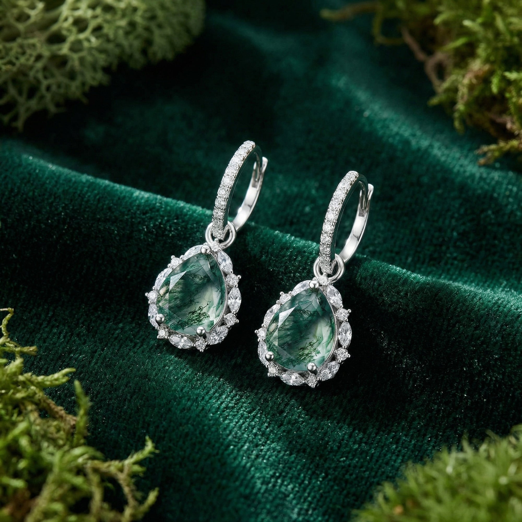 Teardrop moss agate leverback earrings in sterling silver with a halo, resting on green velvet with moss.