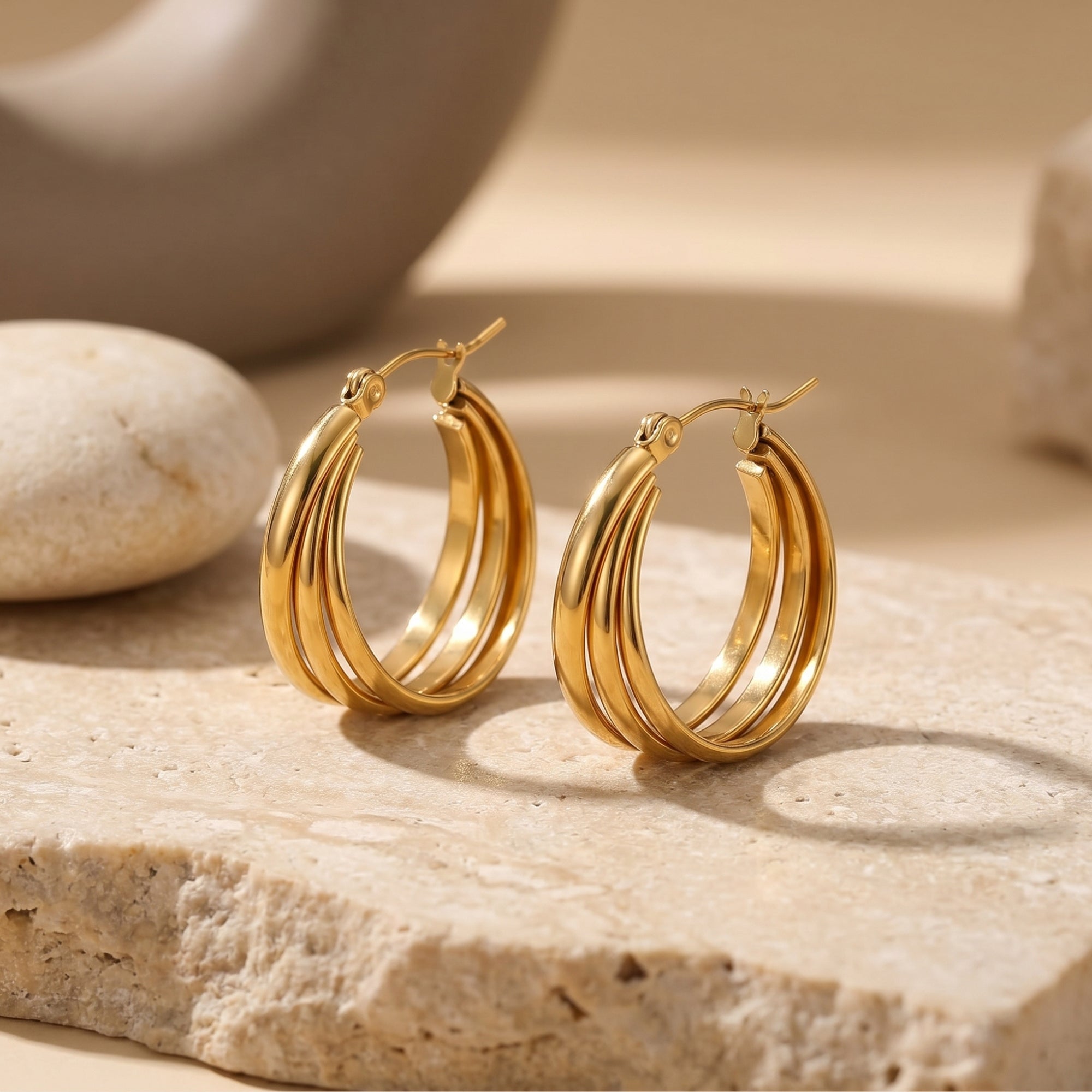 Gold triple-row woven hoop earrings on a textured stone surface.