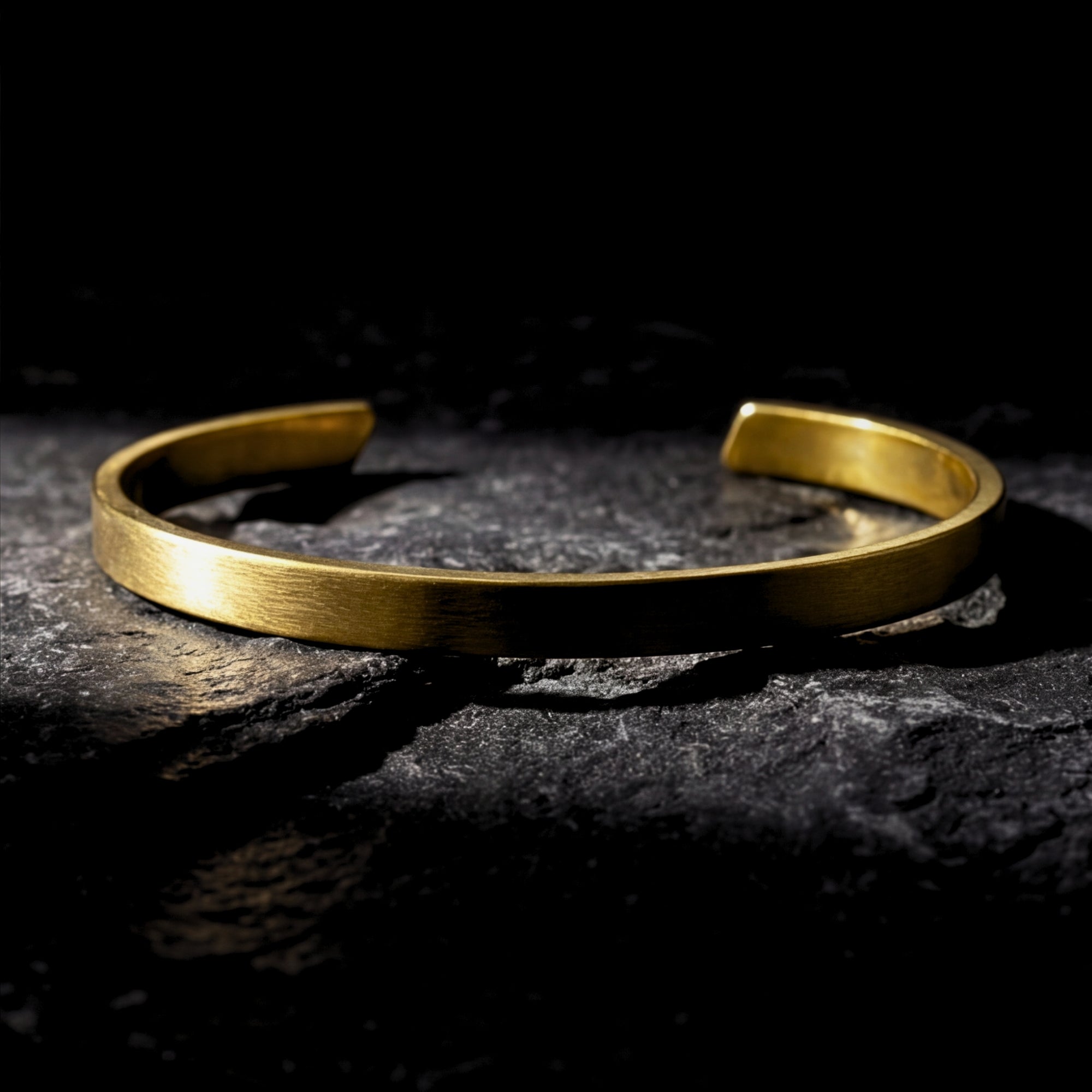 Gold stainless steel Meridian Cuff bracelet lying on a dark, textured rock surface.