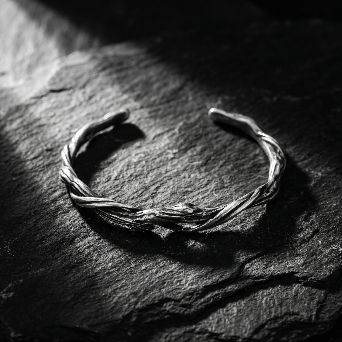 Silver twisted vine cuff bracelet resting on a dark slate surface in dramatic light.