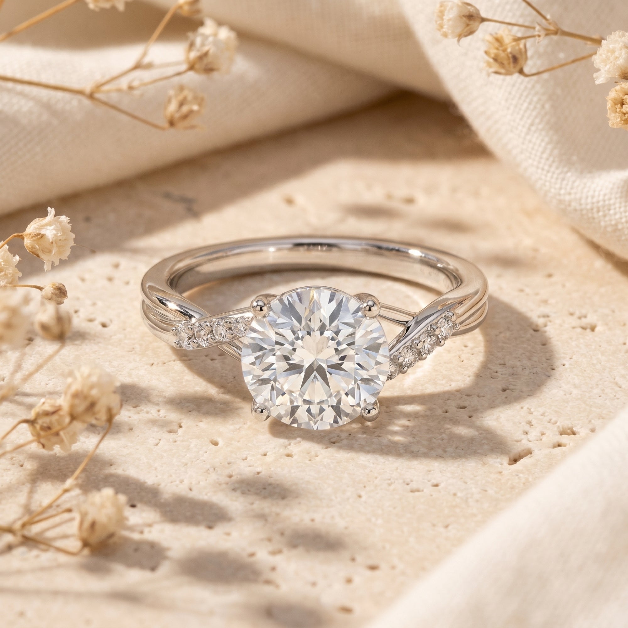 Round cut moissanite promise ring in silver with twisting band on stone surface with dried flowers.