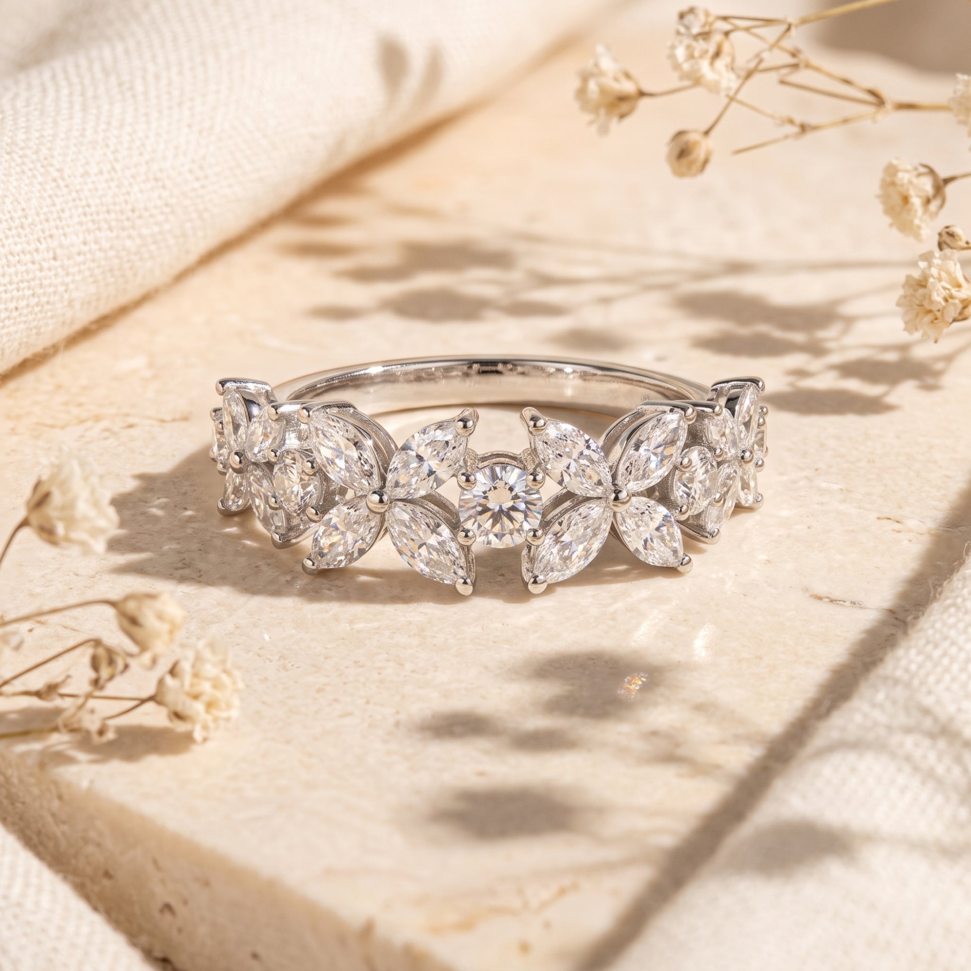 Silver floral cluster promise ring with marquise zircon stones on a stone surface with dried flowers.