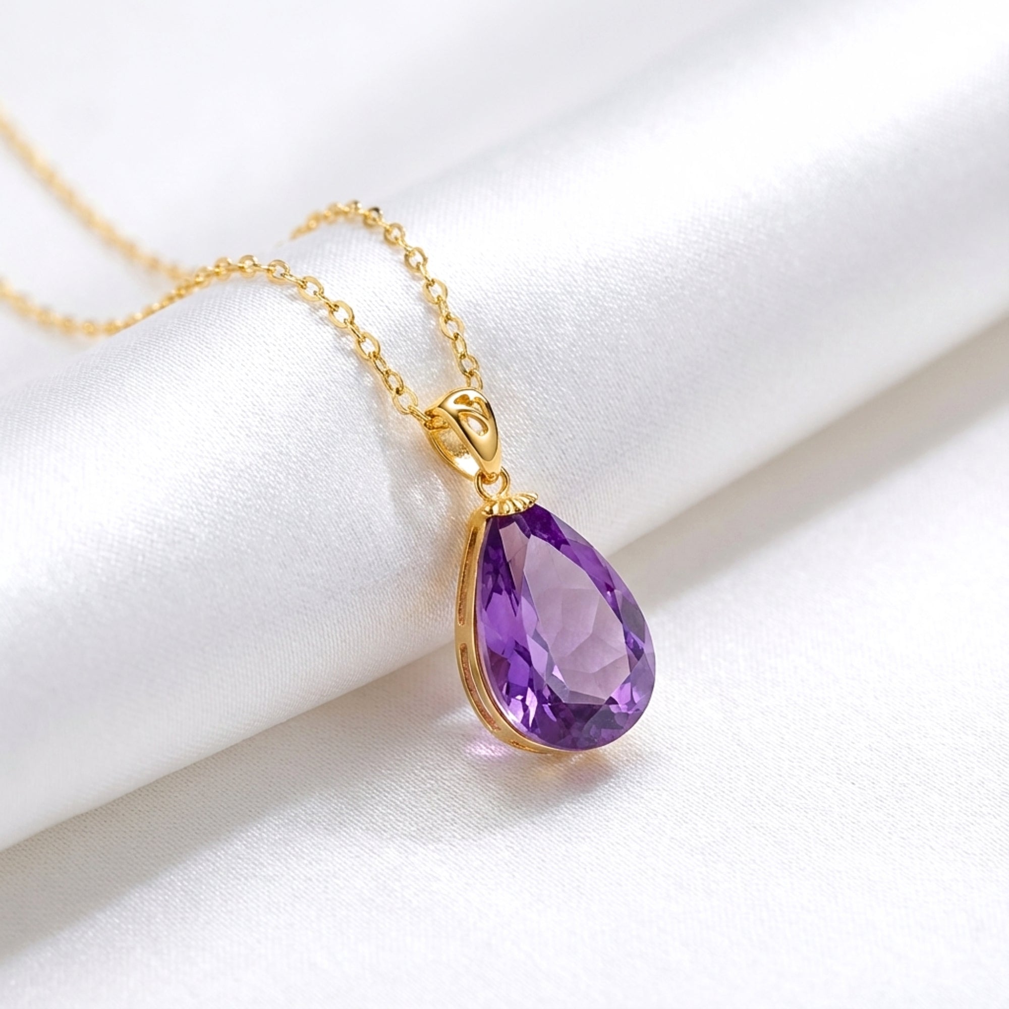 Macro view of a teardrop cut simulated amethyst pendant in 18K gold vermeil on white silk.