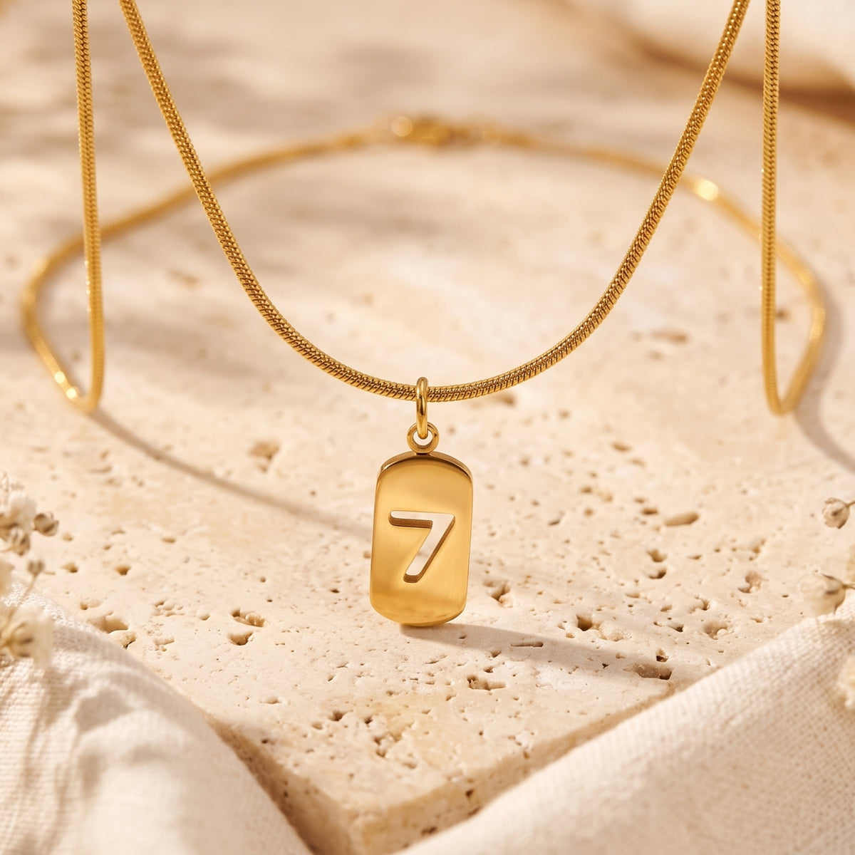 Close-up of a gold-tone snake chain necklace with a rounded tag pendant featuring a cutout number 7.