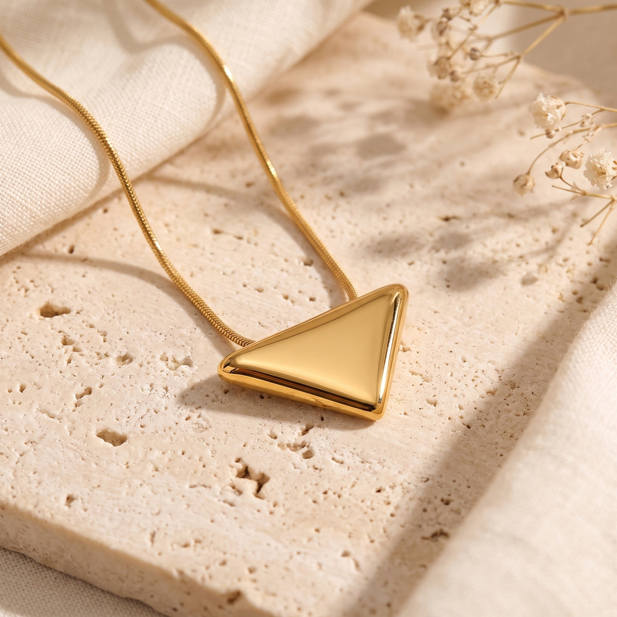 Gold-tone polished triangle pendant necklace resting flat on a textured stone surface.