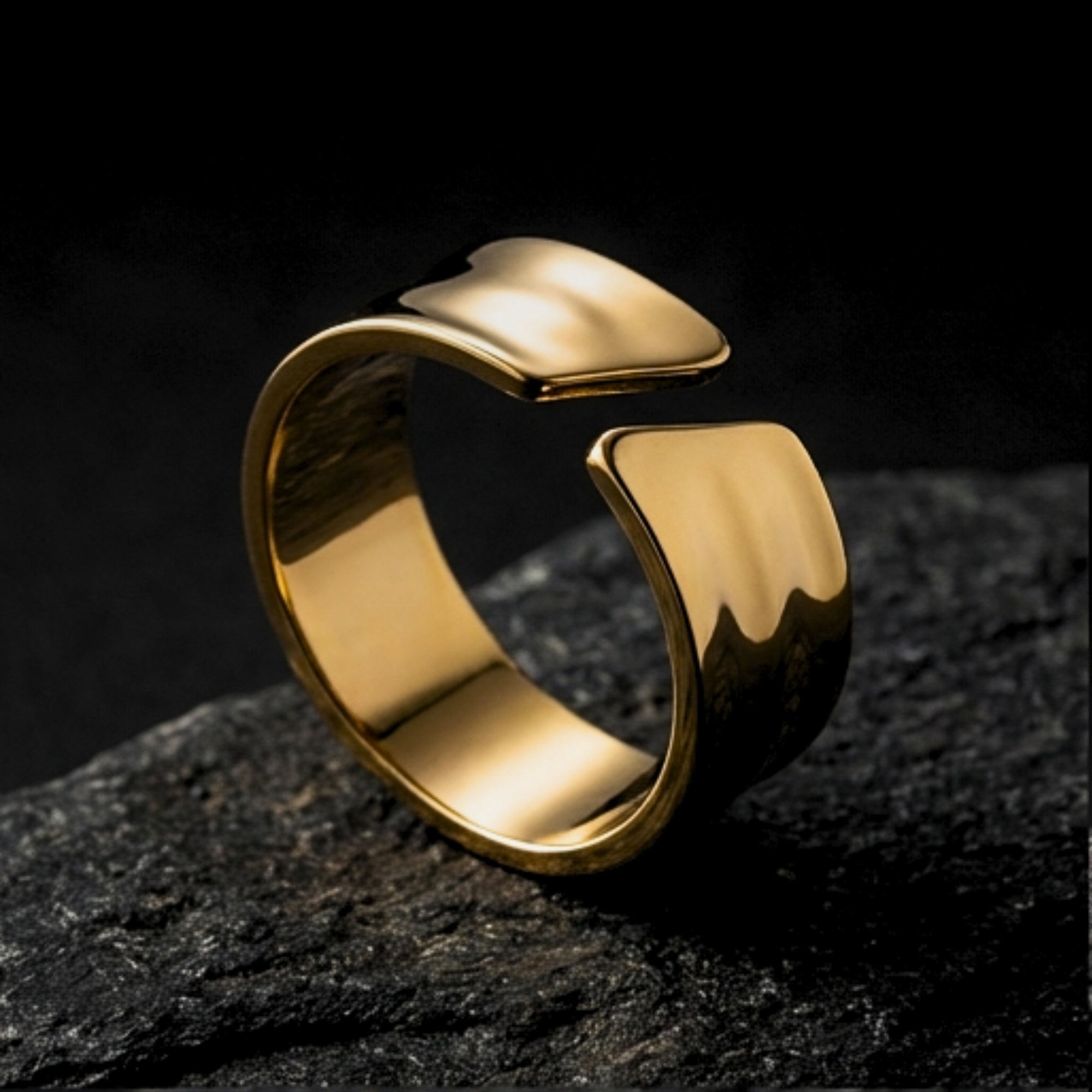 Gold stainless steel Origin Flow ring with an open band design resting on a dark textured rock surface.