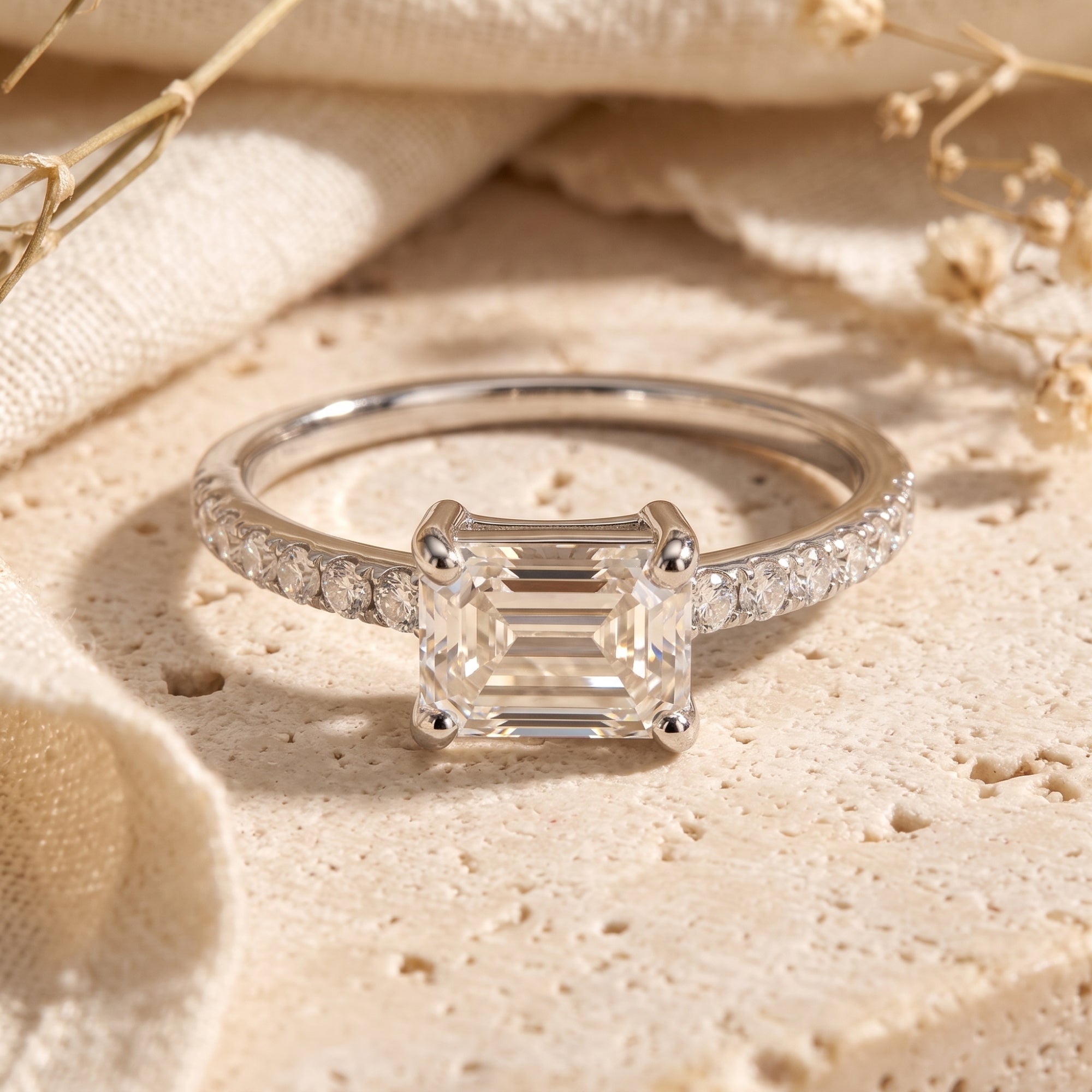 Silver Sarielle East-West ring with a horizontal emerald-cut simulated diamond on a textured stone surface.