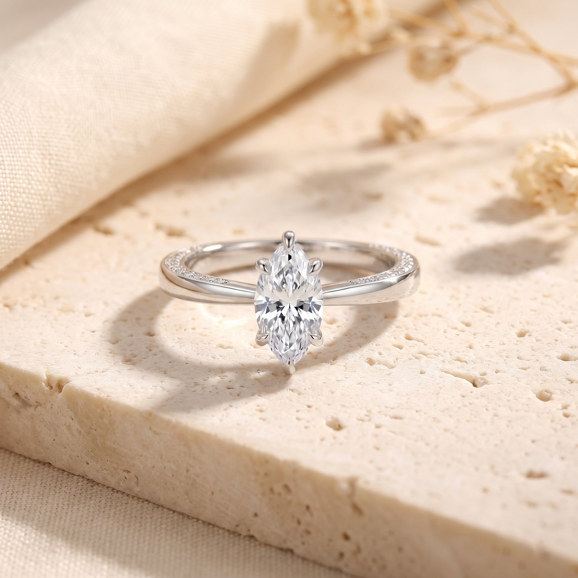 Marquise-cut simulated diamond ring in sterling silver on a textured stone surface with dried flowers.