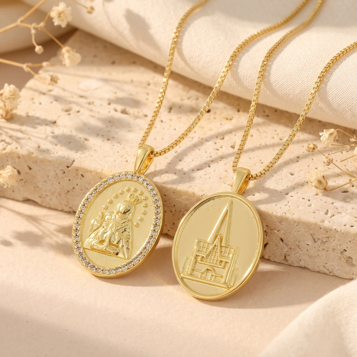 Two gold-tone oval medallion pendants side-by-side displaying the rhinestone Marian side and cathedral side.