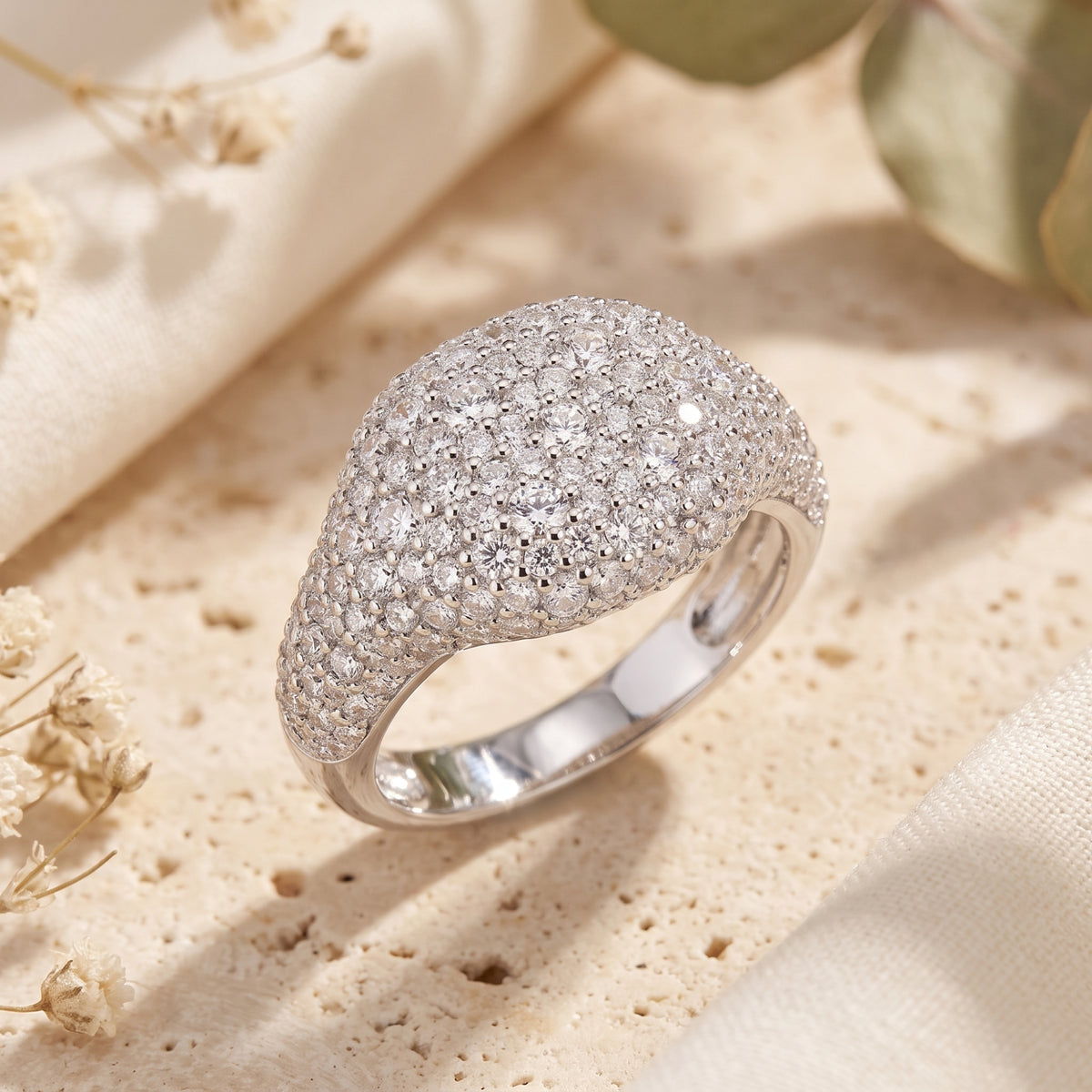 Angled close-up of a solid gold pave dome ring in white gold with round clear simulated diamonds on a textured surface.