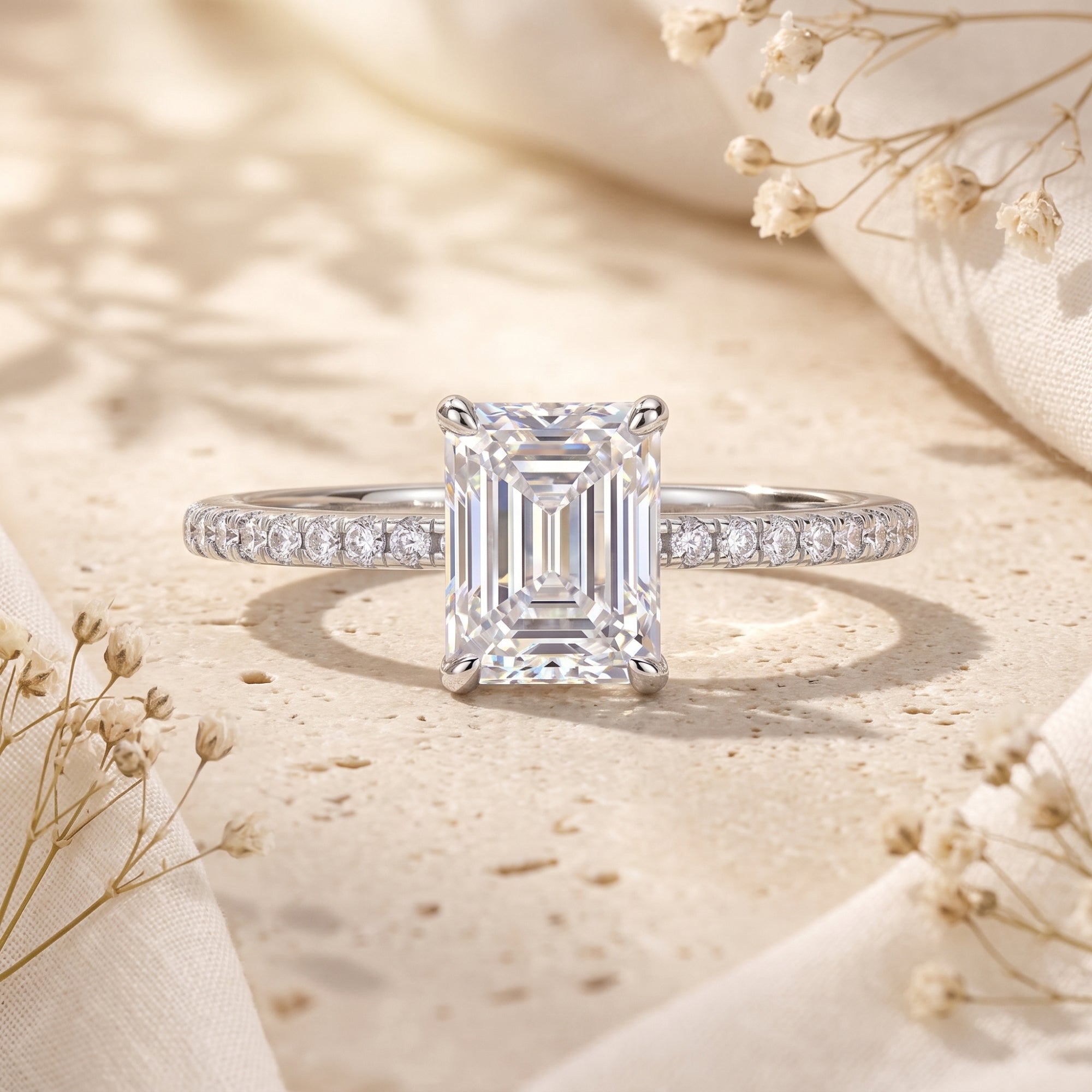 Emerald-cut simulated diamond ring in S925 sterling silver on a stone surface with dried flowers.