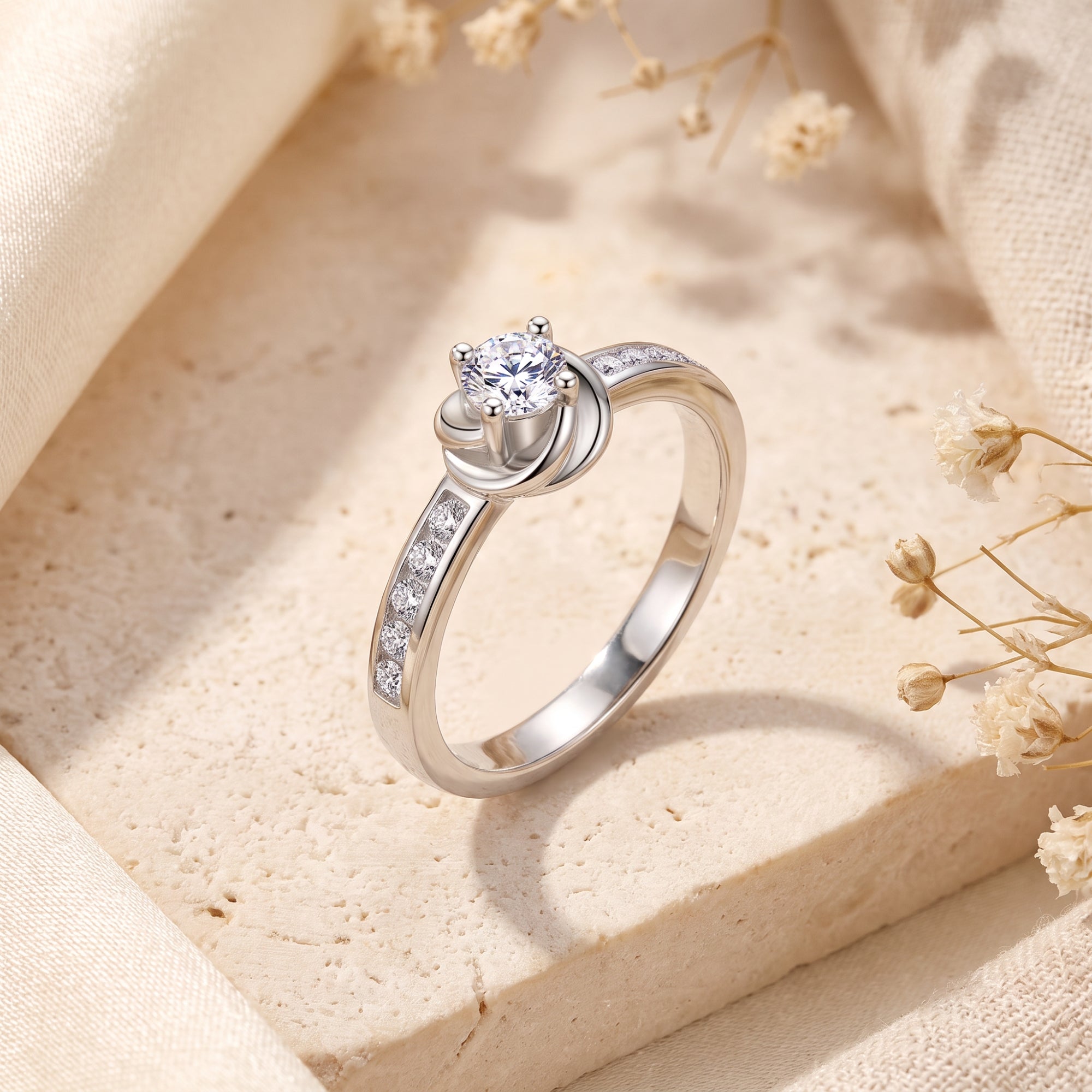 Top view of the silver bypass swirl ring with a round-cut simulated diamond on a stone surface with dried flowers.