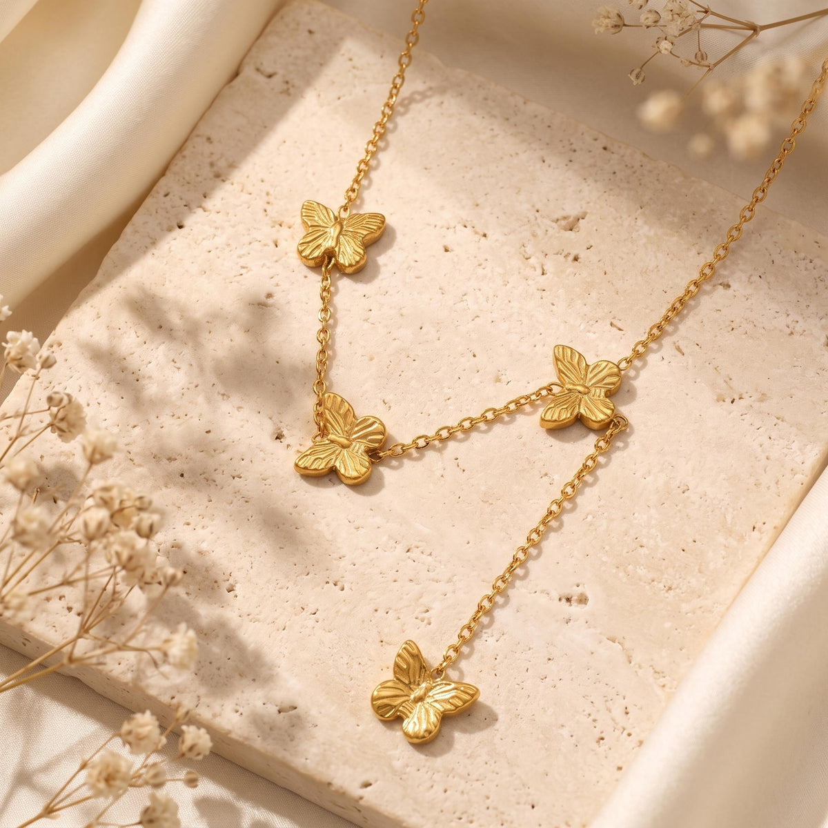 Gold-tone butterfly lariat necklace with four textured butterfly charms laid flat on a stone tile.