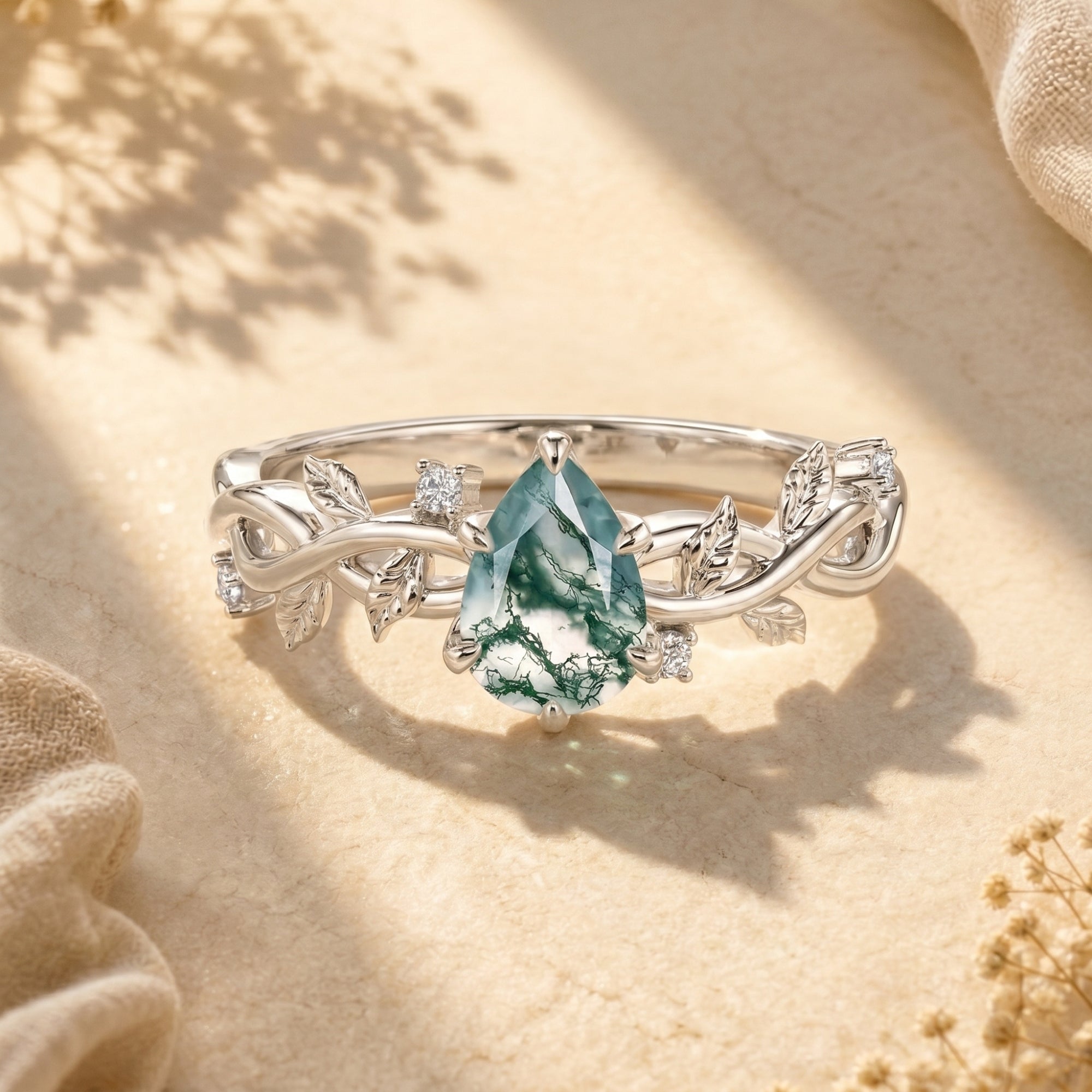 Sterling silver pear-cut moss agate ring with vine band on textured surface.