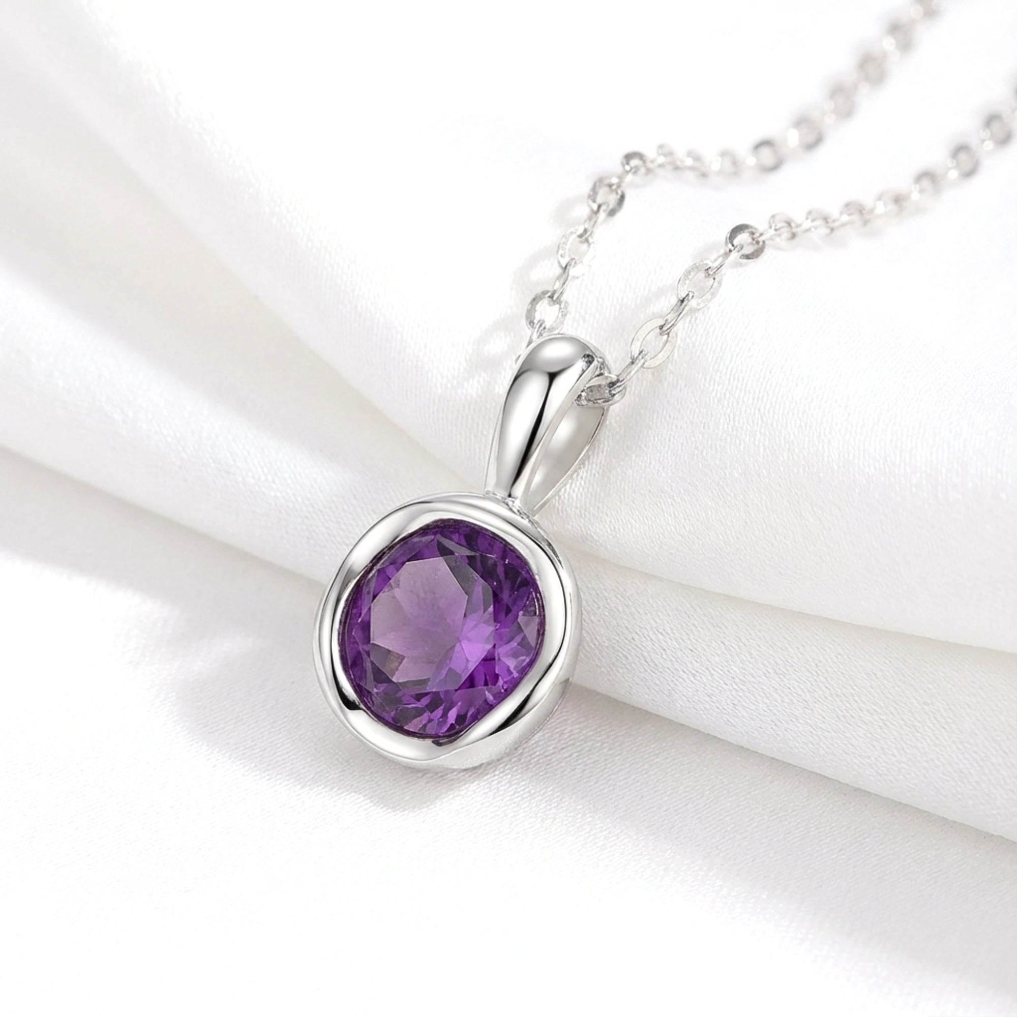 Round cut deep royal purple simulated amethyst solitaire necklace in sterling silver on white silk fabric.