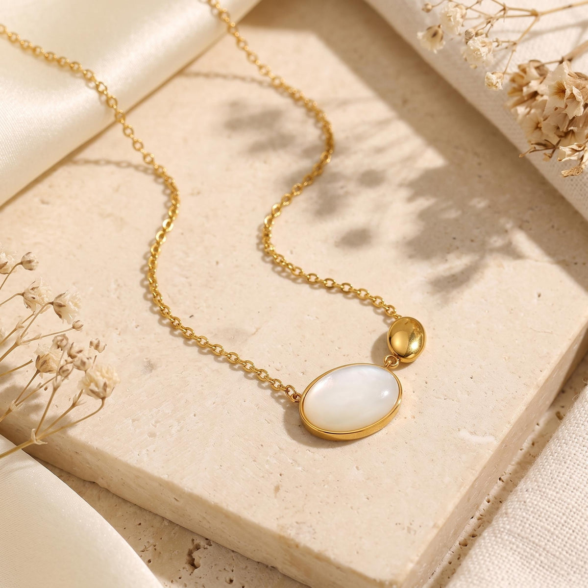 Gold-tone necklace with mother-of-pearl oval cabochon and pebble pendant laid flat on a textured stone slab.