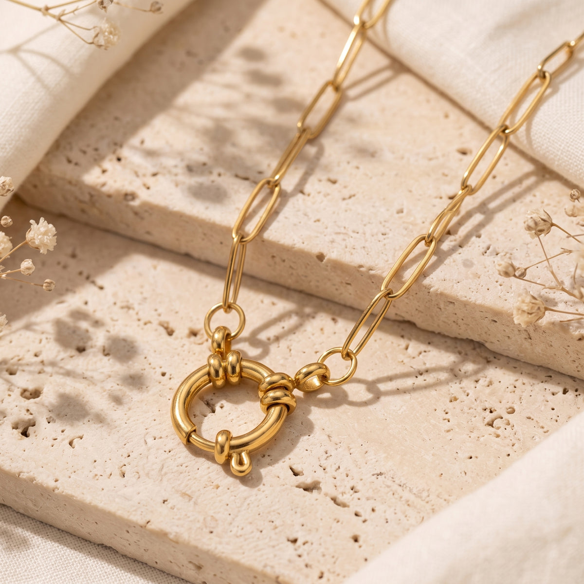 Close-up of the gold-tone paperclip link necklace displaying its central sailor clasp on textured stone.