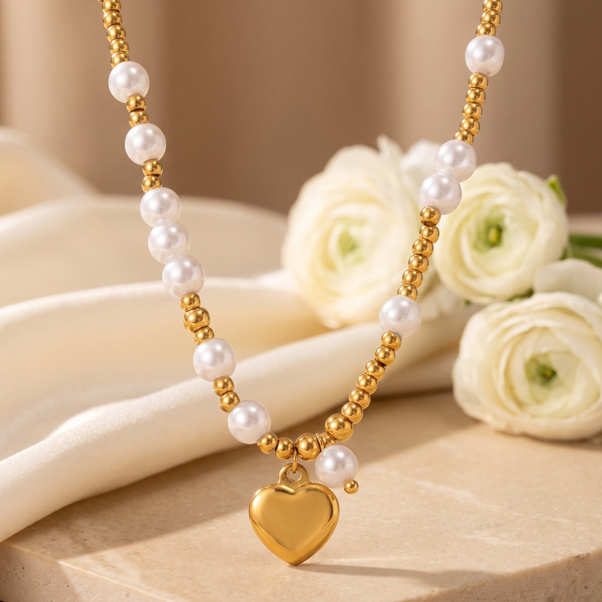 Close-up of a gold-tone pearl heart pendant necklace displayed over cream fabric with white flowers.