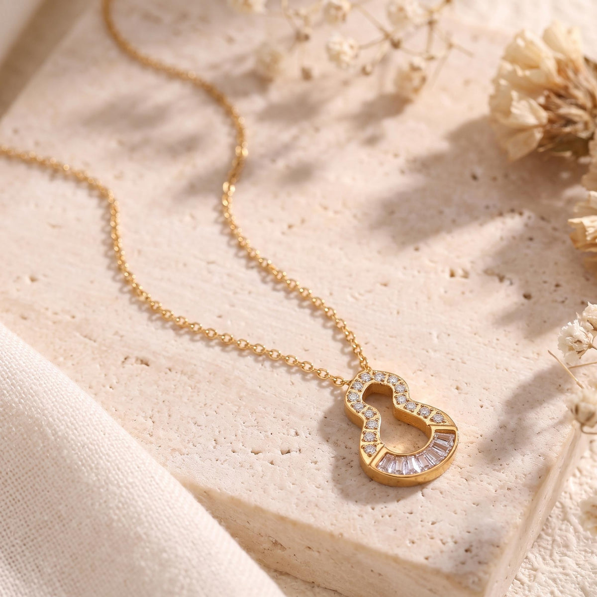 Close-up of the gold-tone keyhole pendant with clear round and baguette stones on a beige stone block.