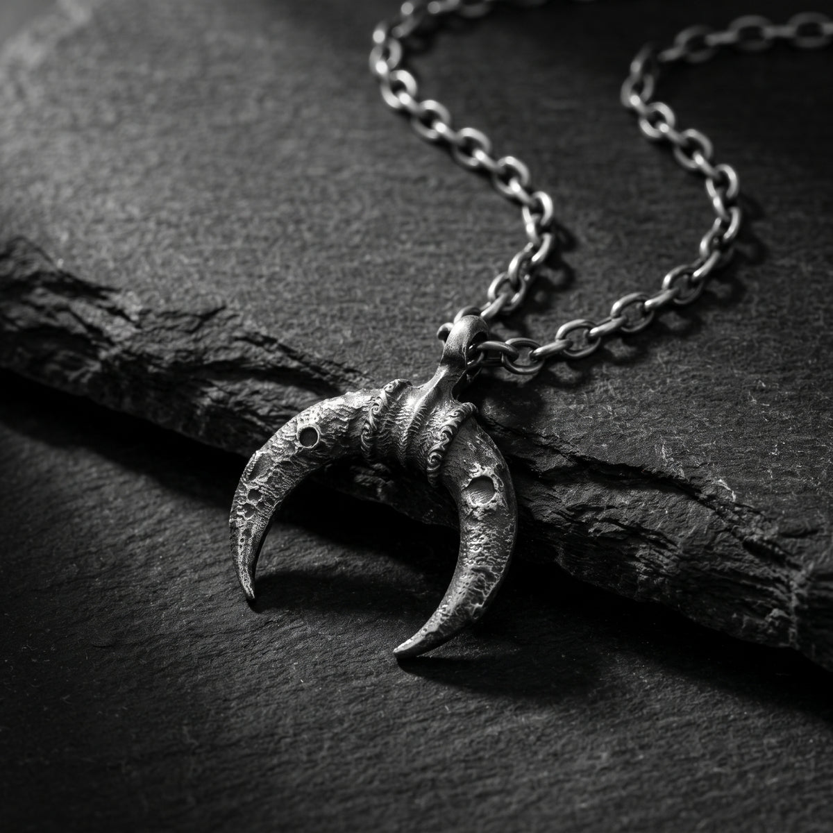 Textured silver crescent pendant and chain resting on a dark slate surface.