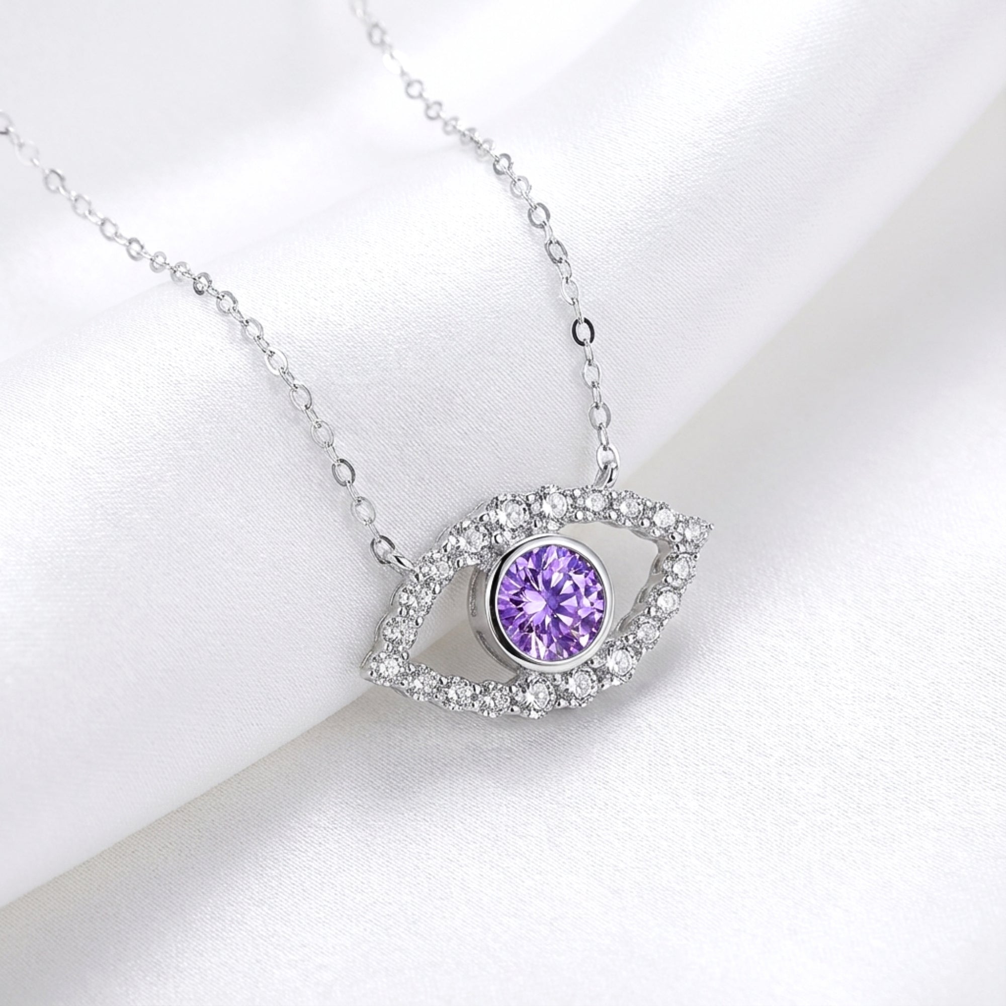 Sterling silver evil eye necklace with a round purple amethyst and moissanite halo on white silk fabric.