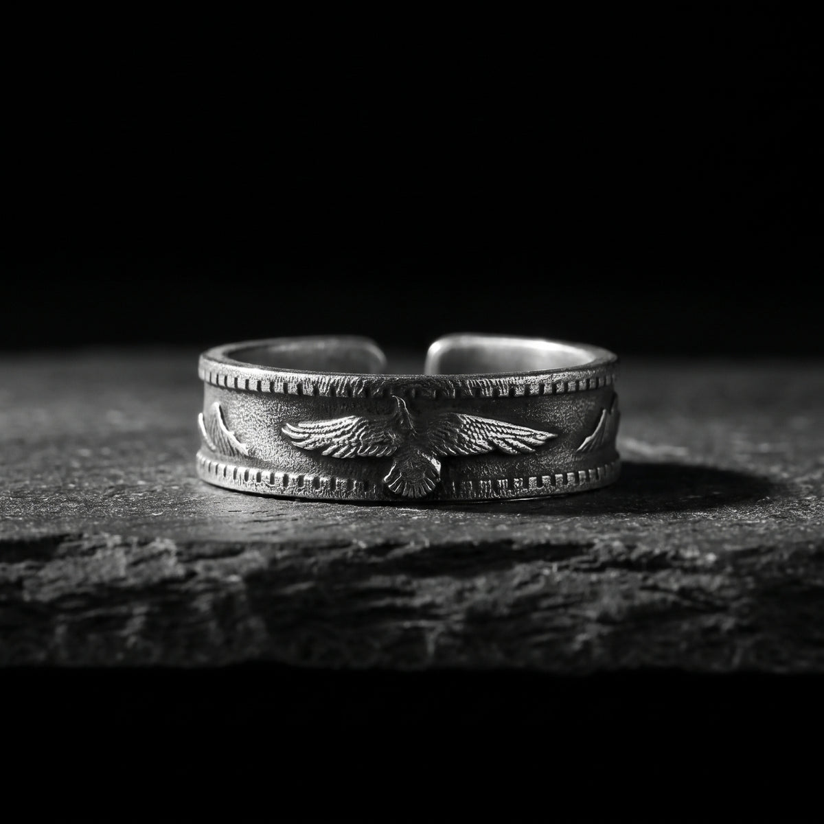 Front view of a silver open-band ring with an eagle relief on a dark slate surface.