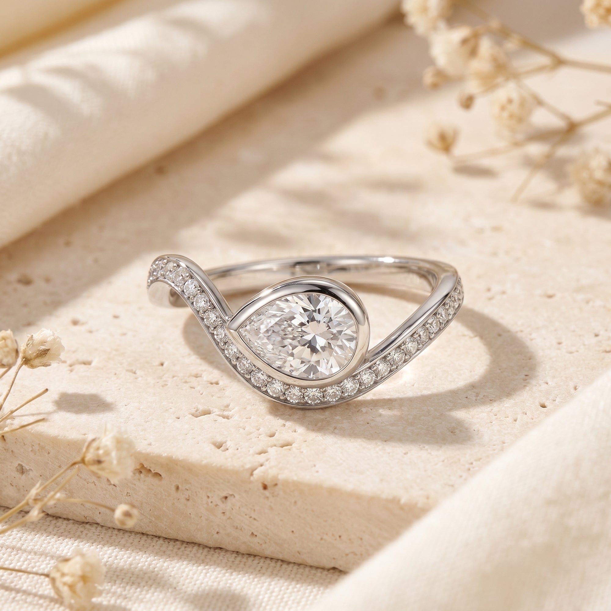Silver pear-cut moissanite bypass ring on stone with dried flowers.