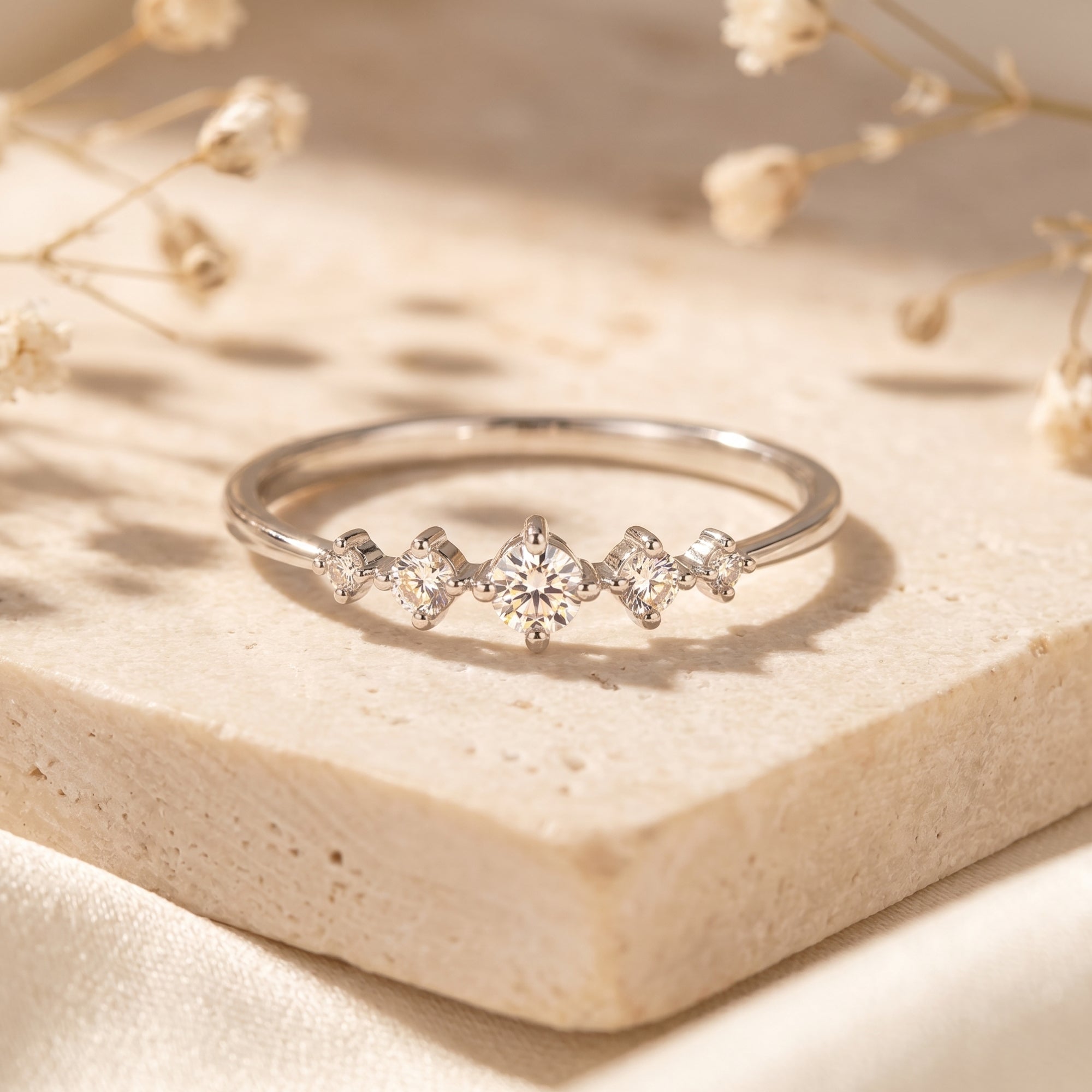 Silver moissanite ring with five round stones on stone with flowers.