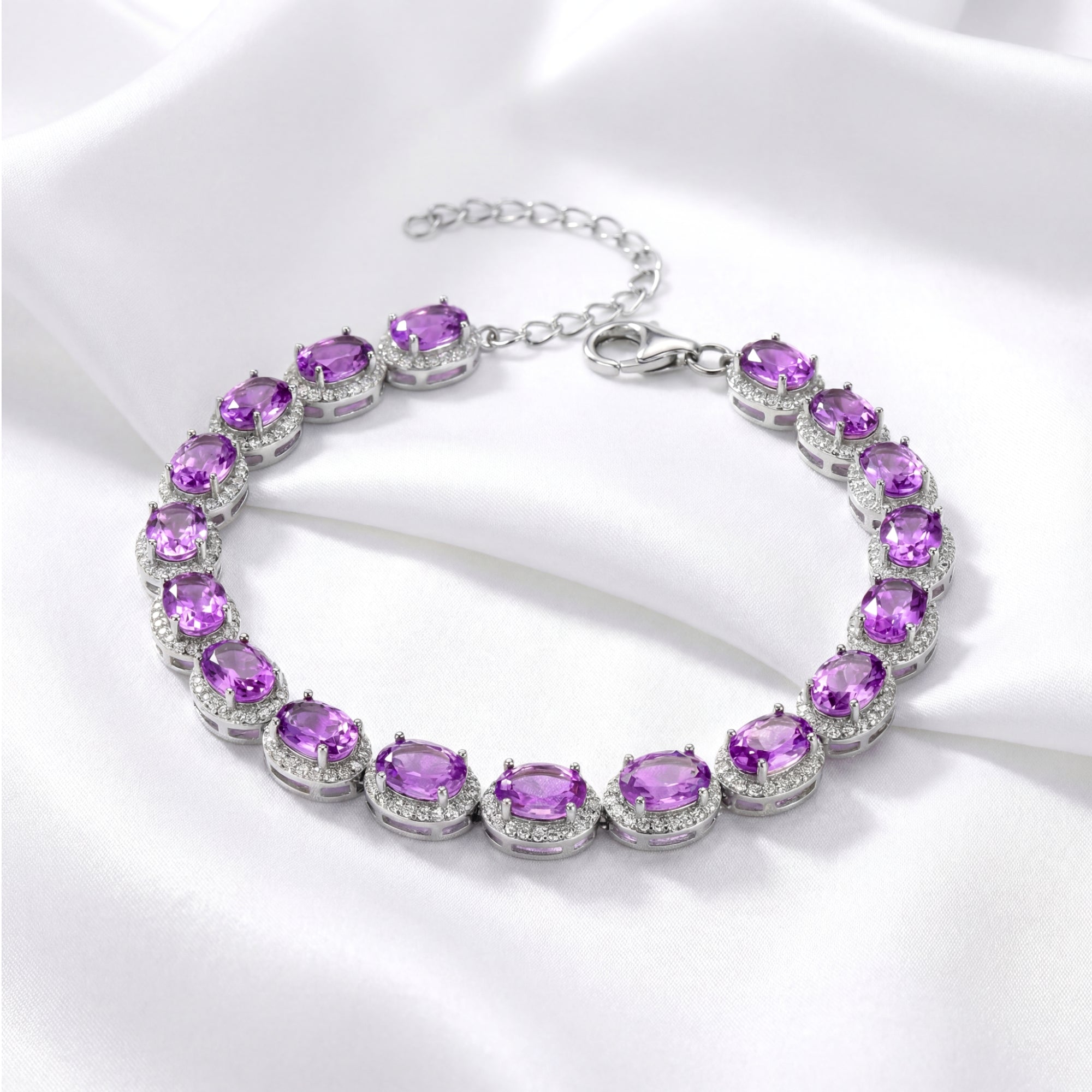 Oval-cut simulated amethyst halo bracelet in S925 sterling silver laid on white silk fabric.
