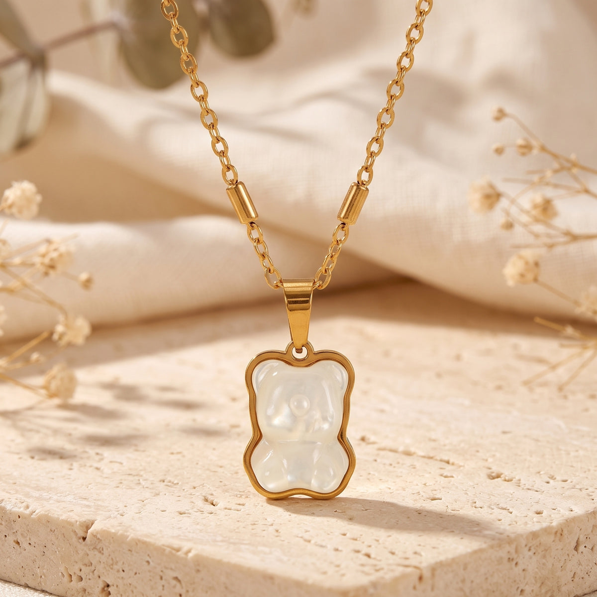 Front view of a gold-tone bear pendant with a pearlescent inset, suspended on a chain over textured stone.