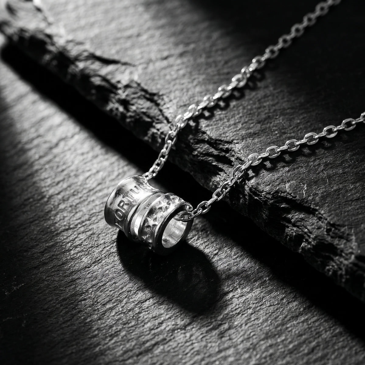 Silver dual-cylinder pendant necklace with engraved lettering and stars resting on dark slate stone.