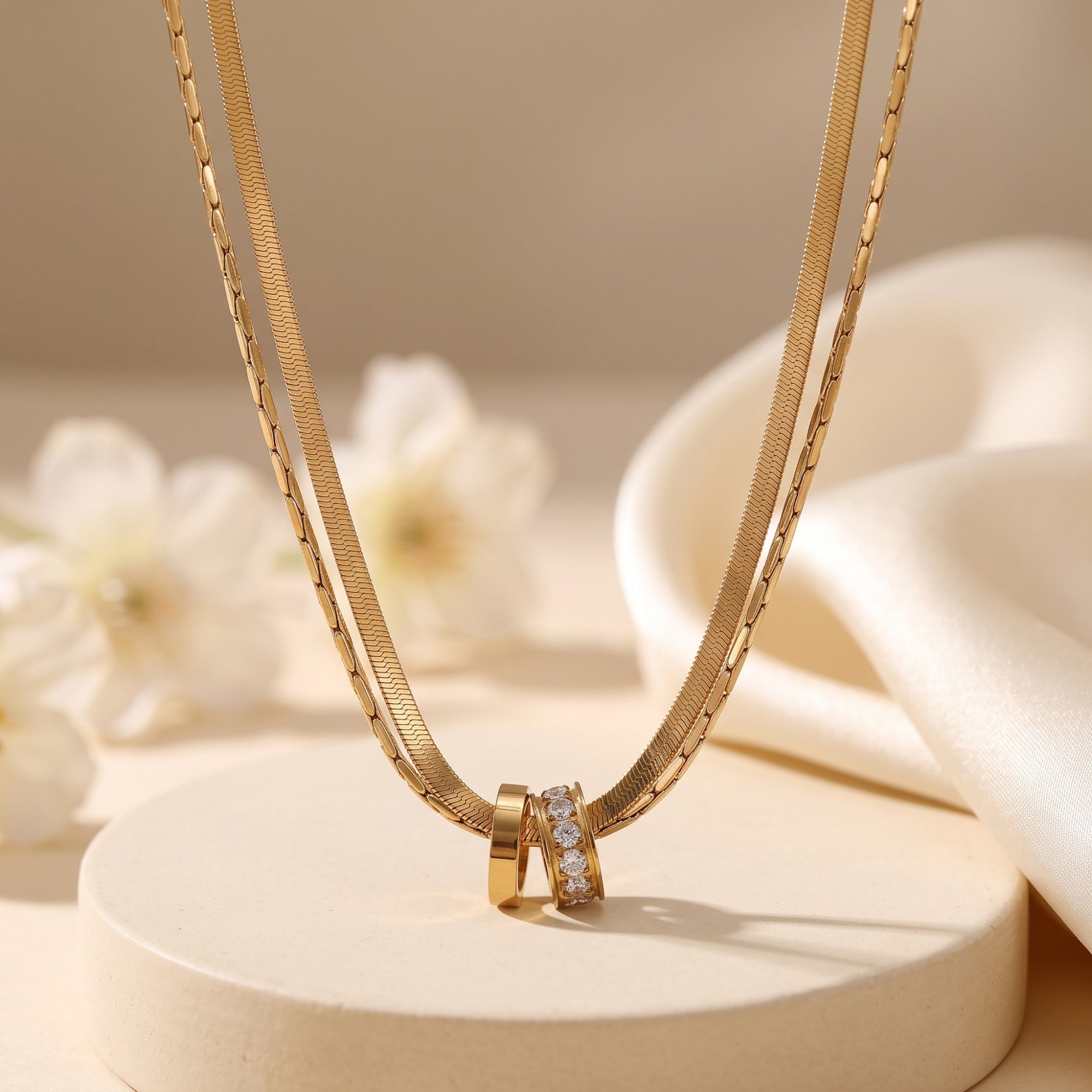 Gold layered necklace with CZ interlocking rings on a pedestal with floral accents.