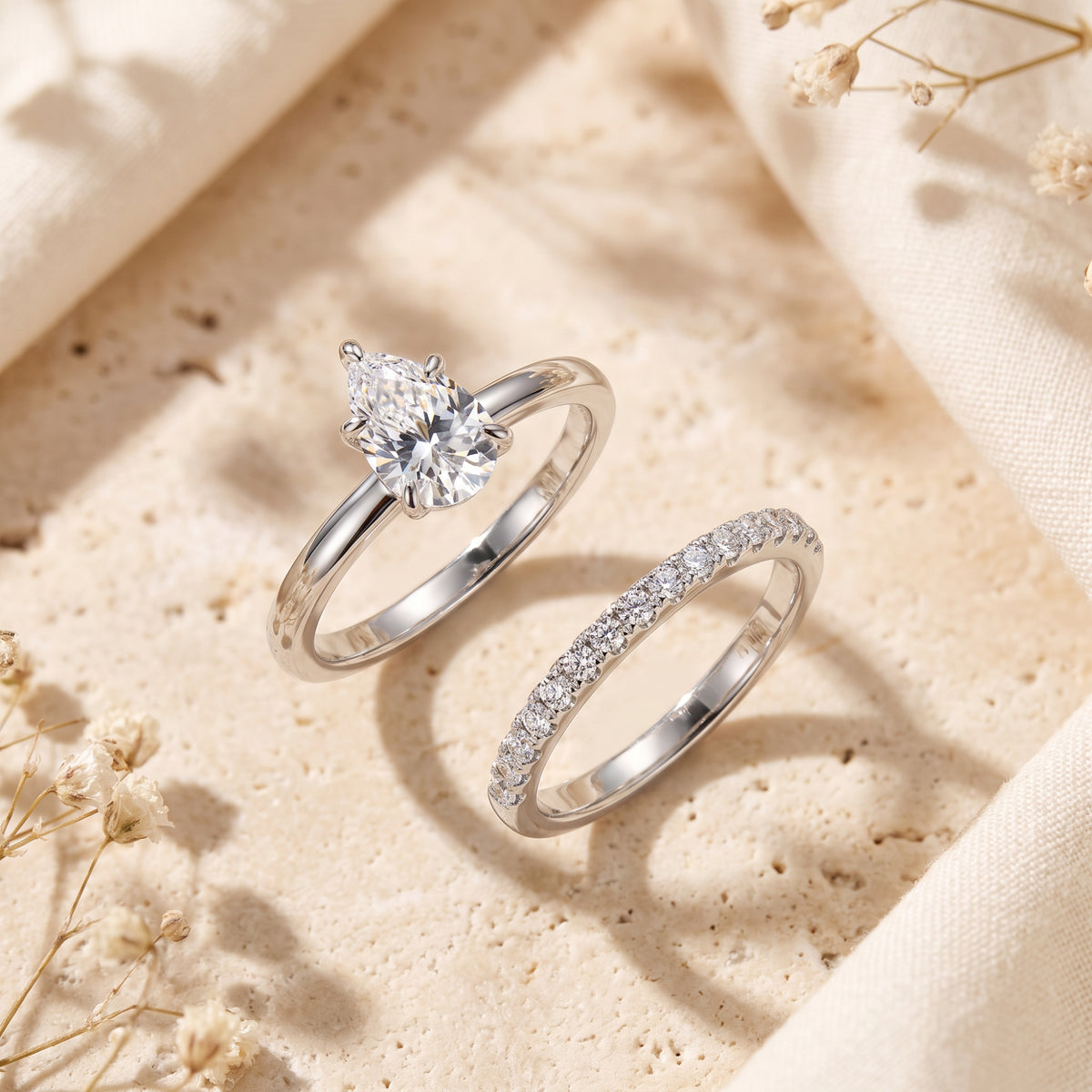 Silver-toned pear-cut solitaire ring and pavé band displayed side by side on a textured stone surface.