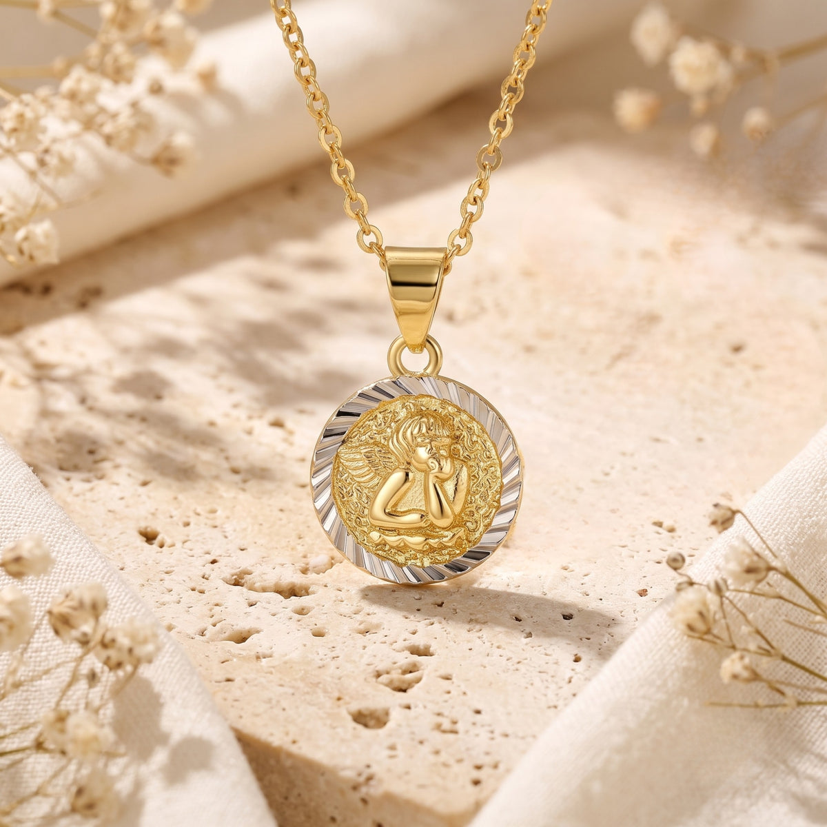 Gold-tone circular cherub medallion with a silver-tone textured rim on a chain over porous stone.