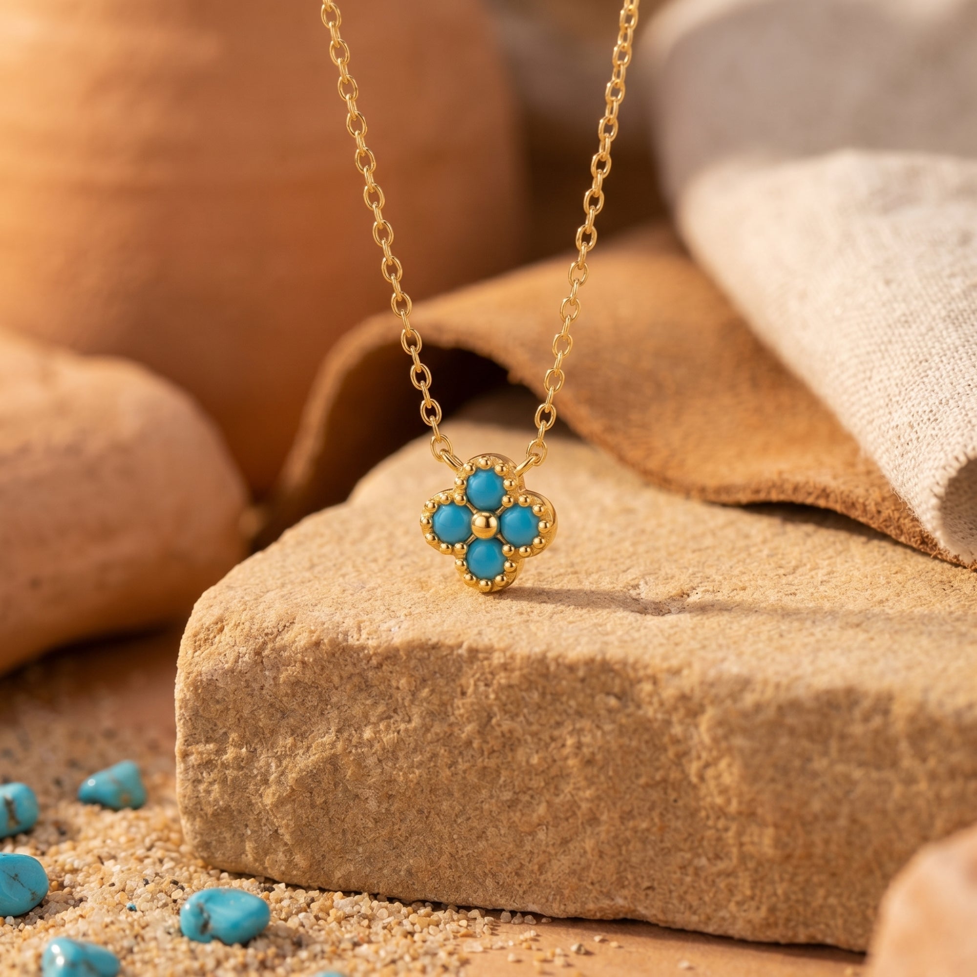 Gold flower pendant necklace with four turquoise cabochons resting on a desert stone.