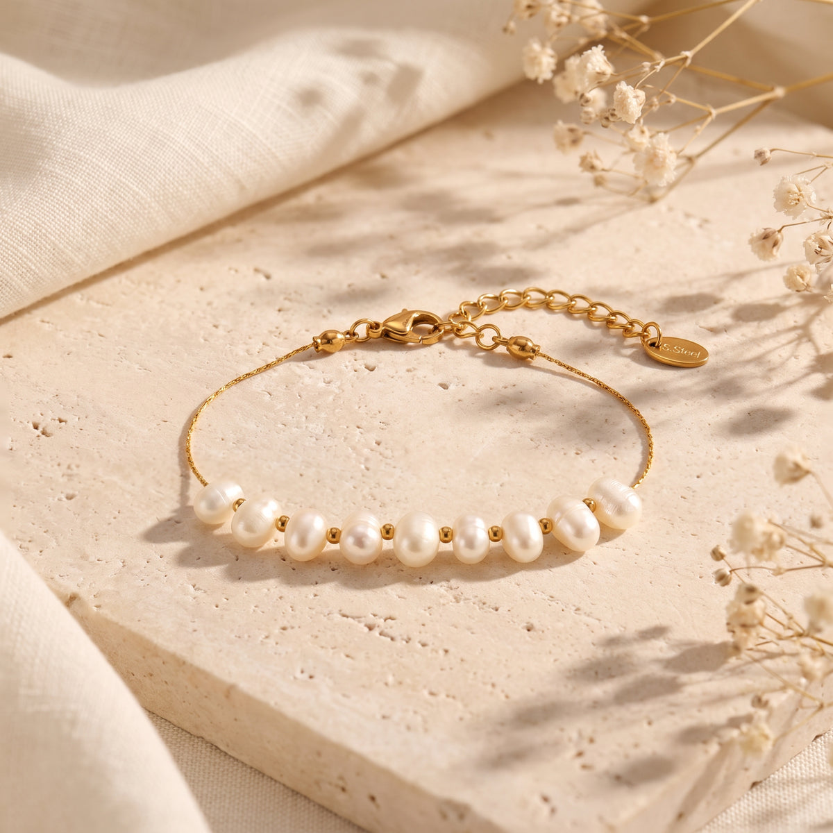 Gold-tone pearl station bracelet arranged in a loop on a light stone slab, with clasp and extender chain visible.