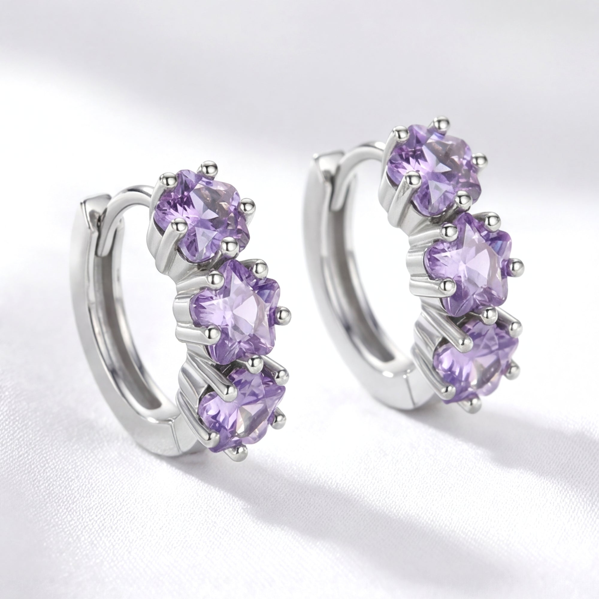 Angled view of S925 sterling silver huggie earrings with three star-cut purple simulated amethysts.