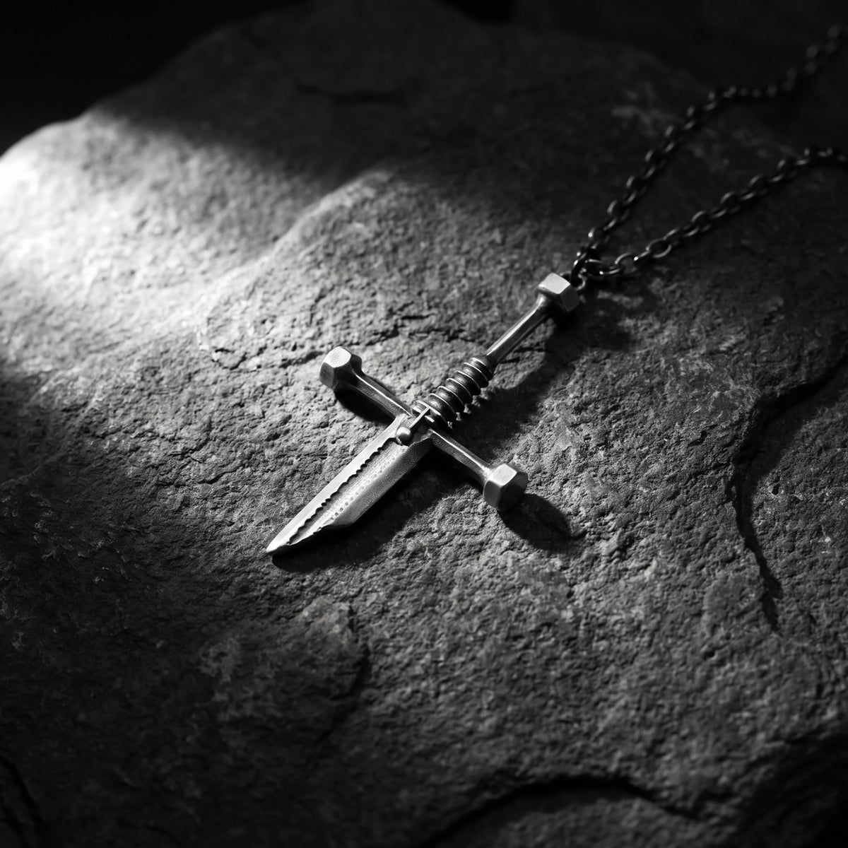 Silver dagger pendant and chain lying diagonally on a rough dark rock surface.